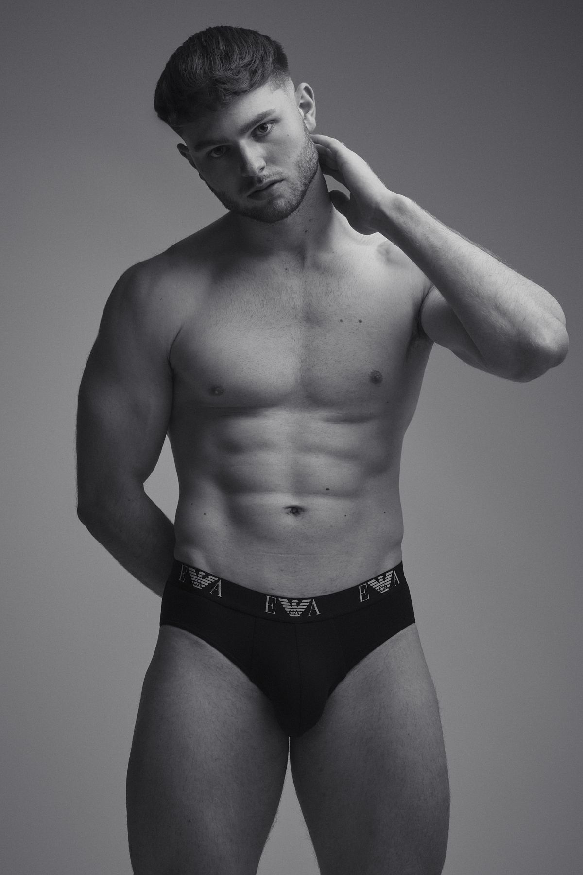 Black-and-white shot of a muscular male model in Emporio Armani briefs, posed confidently against a neutral backdrop