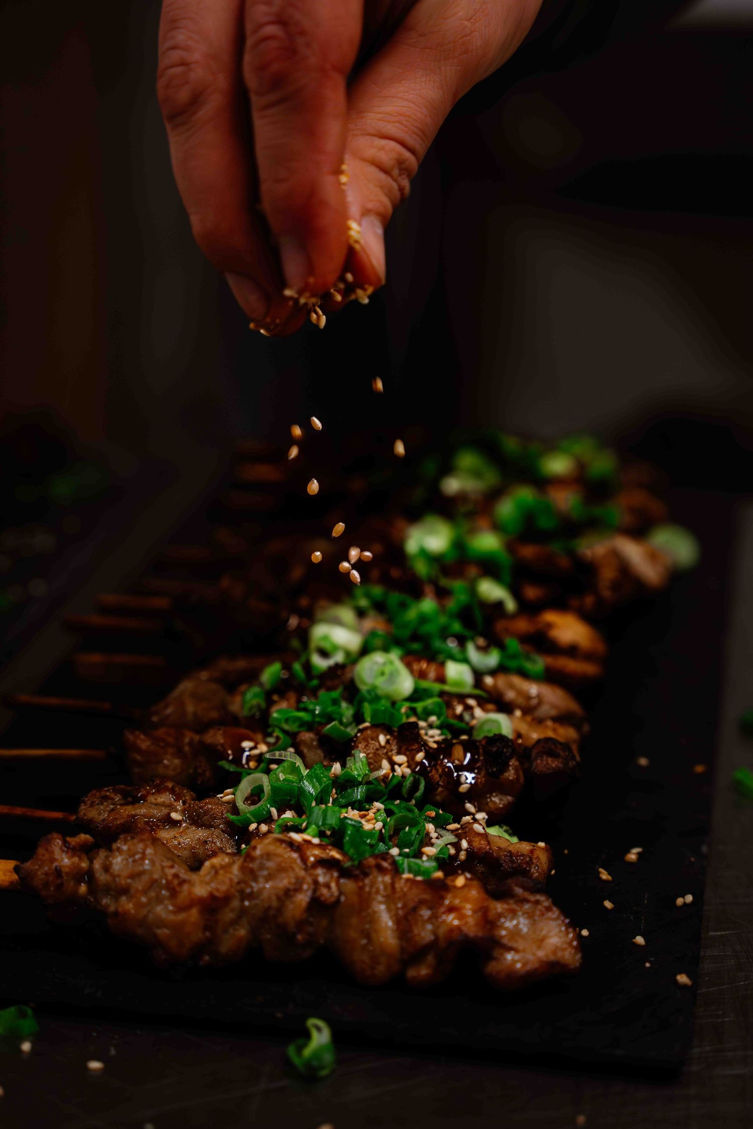 Seasoning being sprinkled over grilled meat garnished with fresh green herbs.