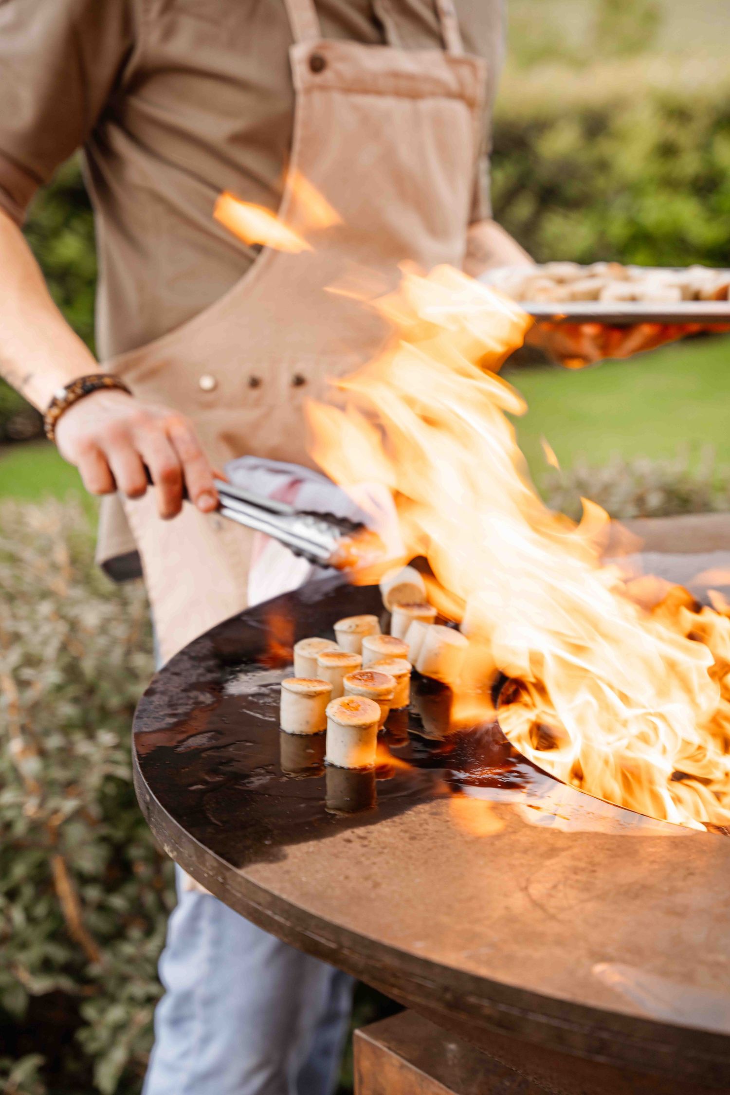 Chef cooking with dramatic flames on an outdoor grill surface.