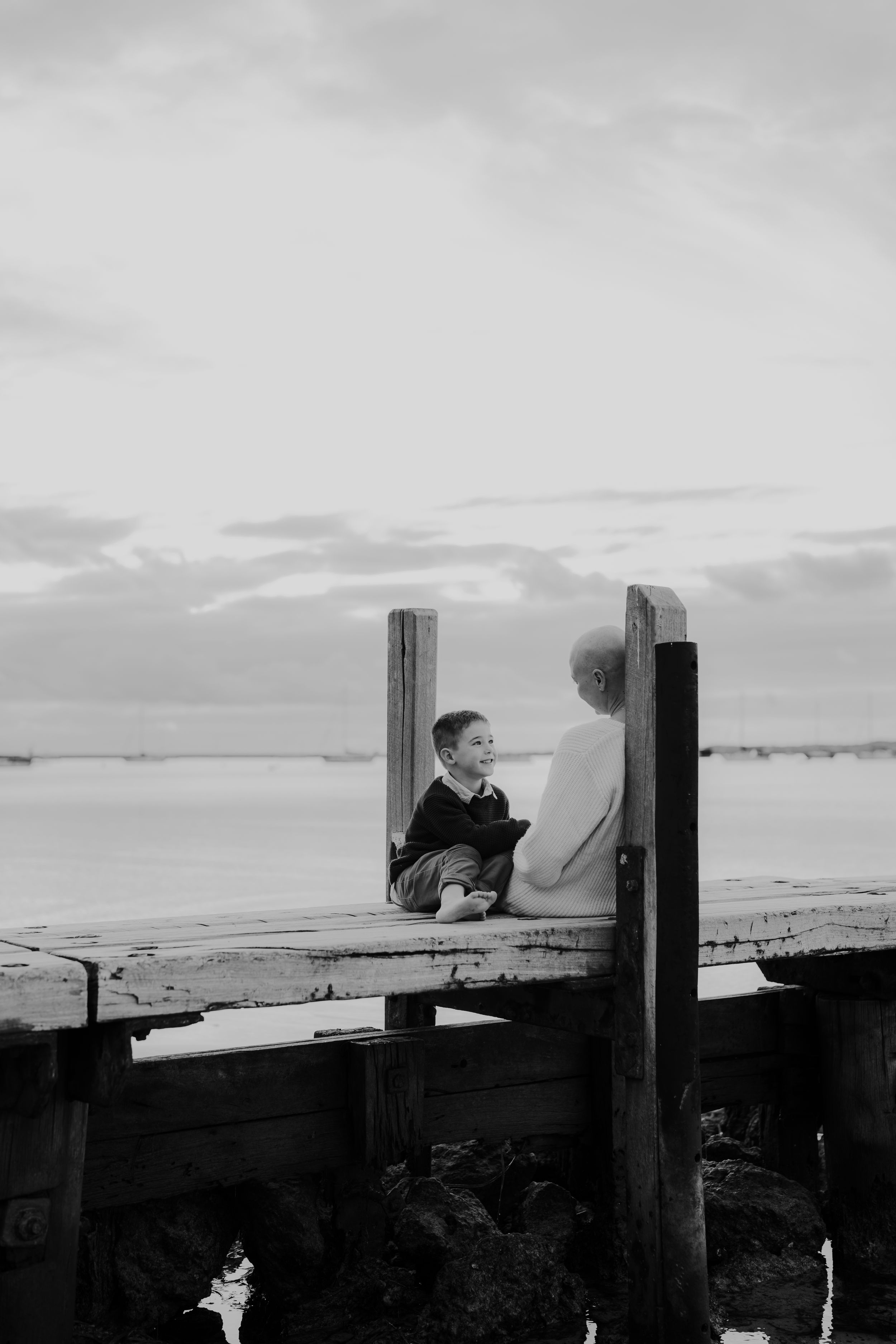Silhouettes of people sitting on wooden deck overlooking scenic ocean view at sunset.