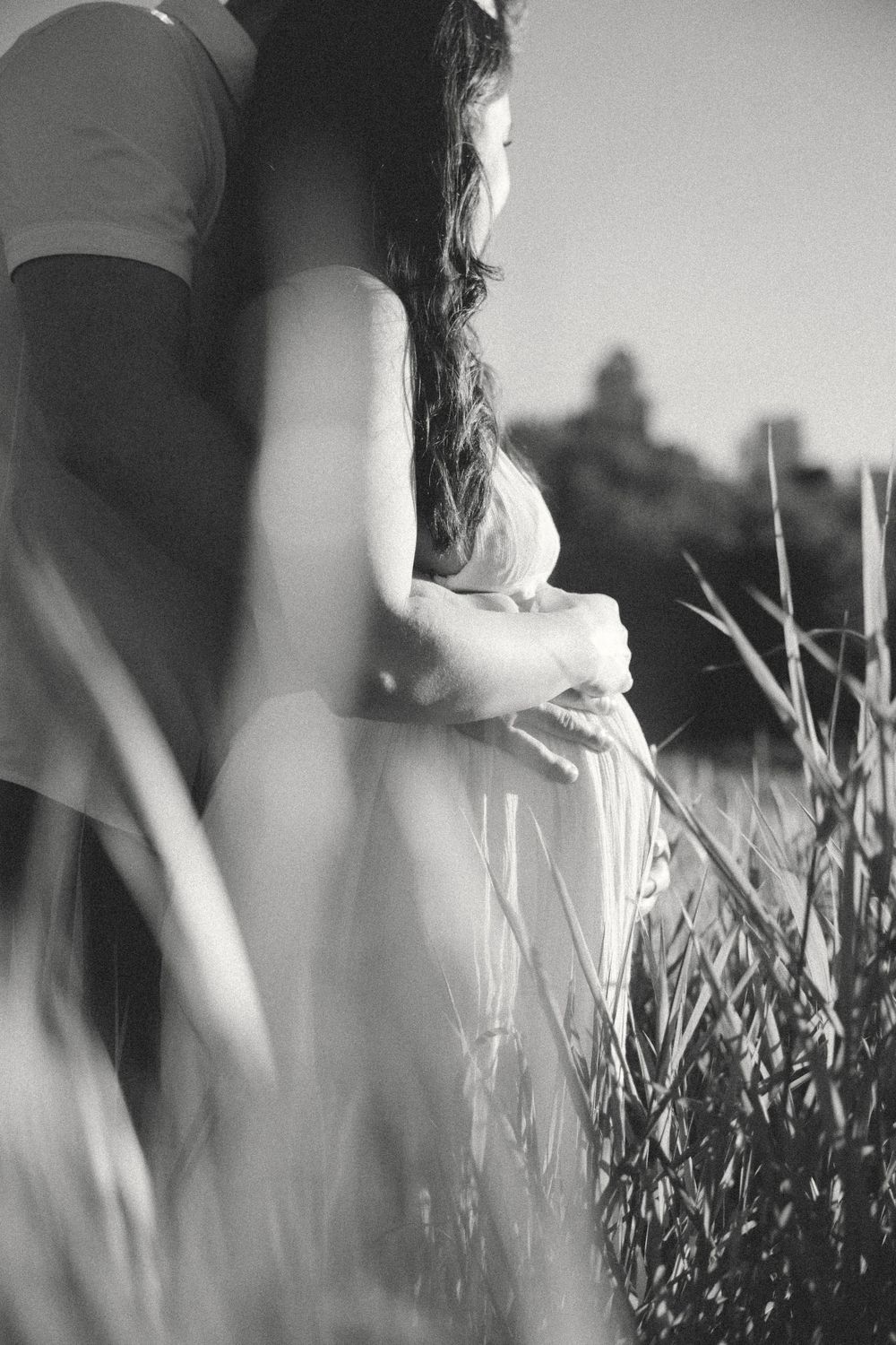 black and white photo of a couple looking into the sunset together while holding the baby belly of the mom during a vancouver maternity sesh