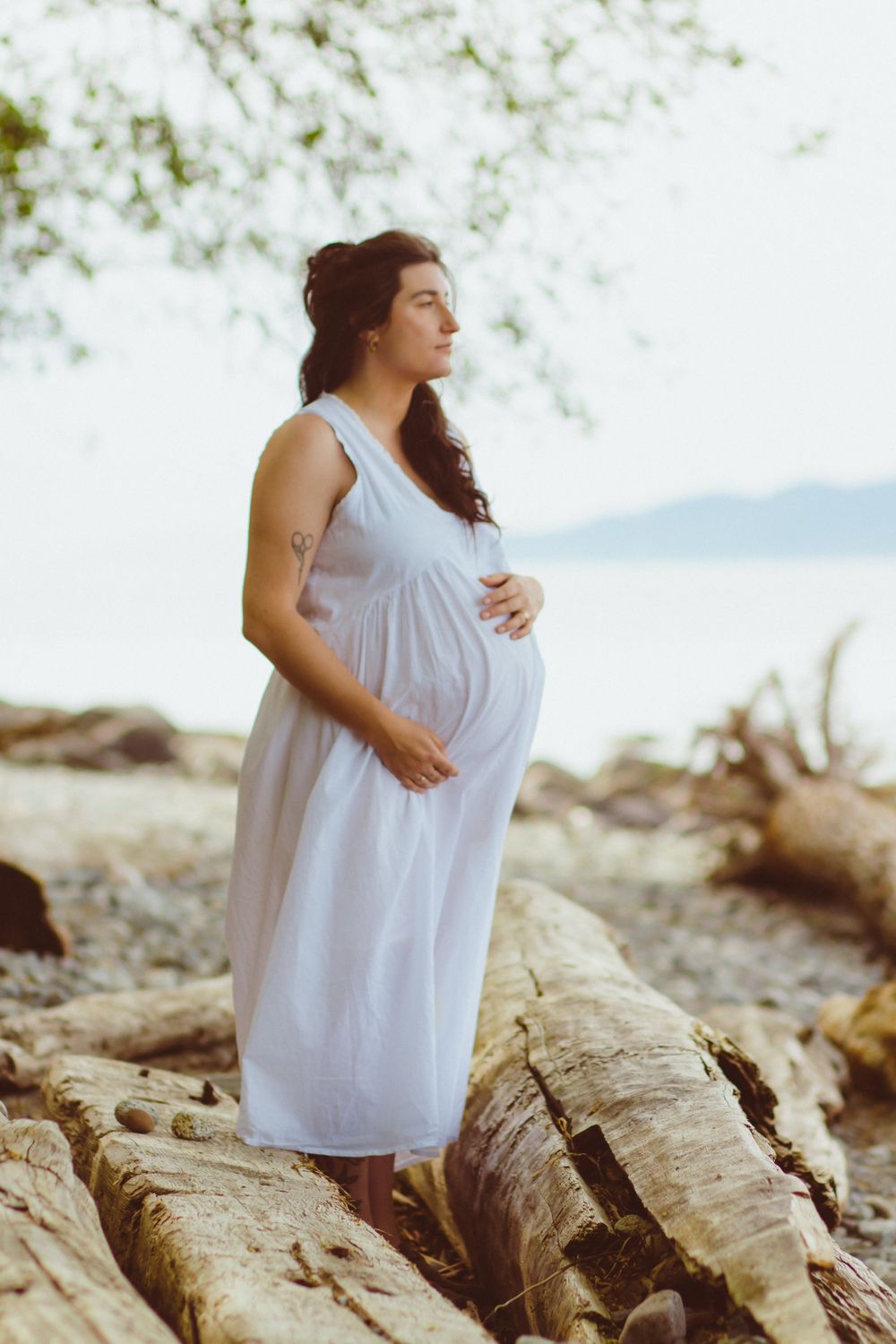 Flowing white dress on expecting mom looking out over the ocean during a vancouver maternity photo session.