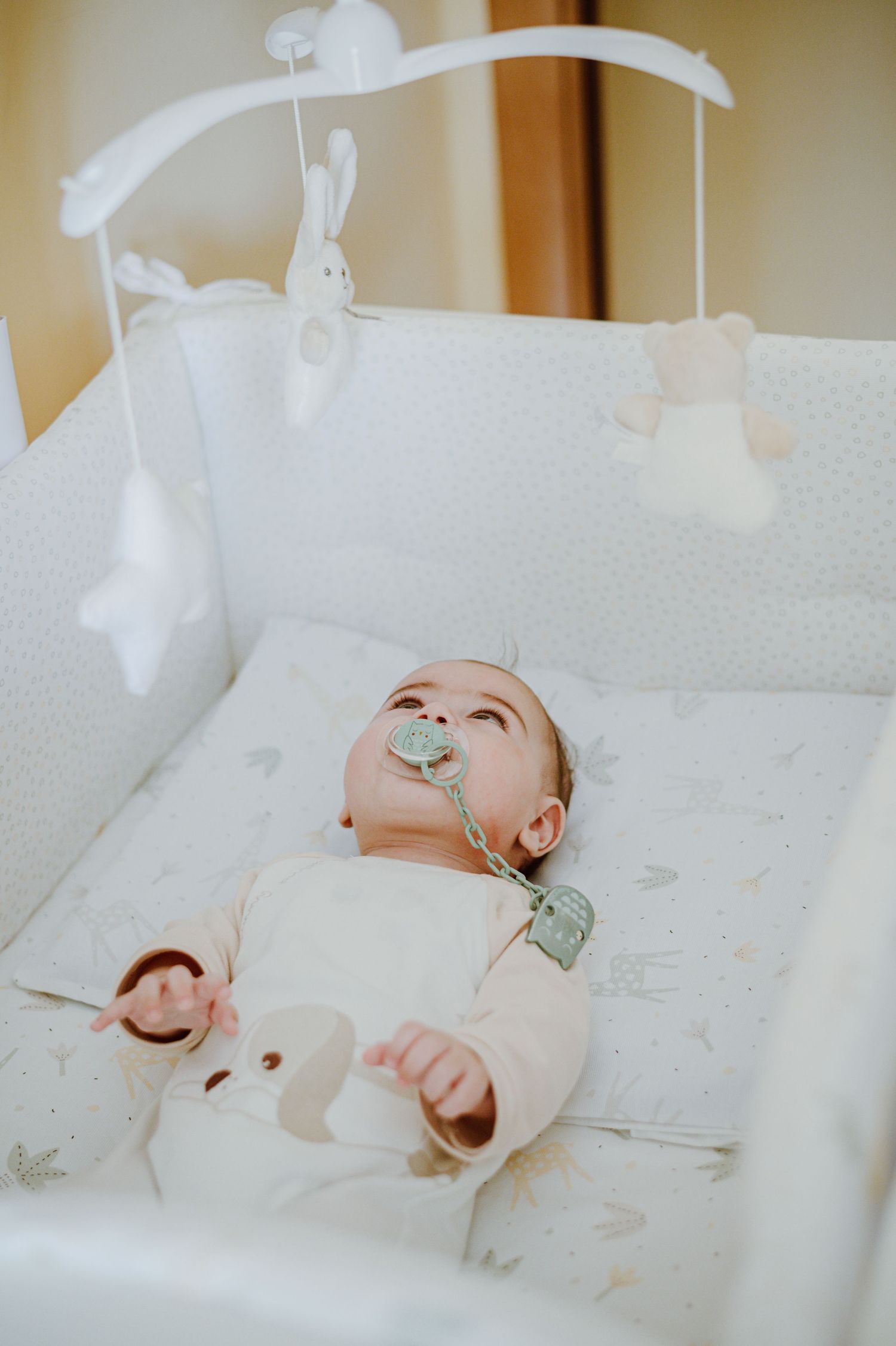 Baby lying under white mobile with bunny and star decorations.