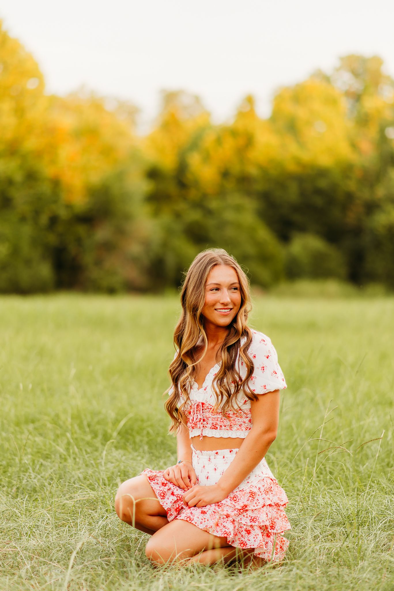 Portrait in a grassy field with autumn trees creating a golden backdrop.