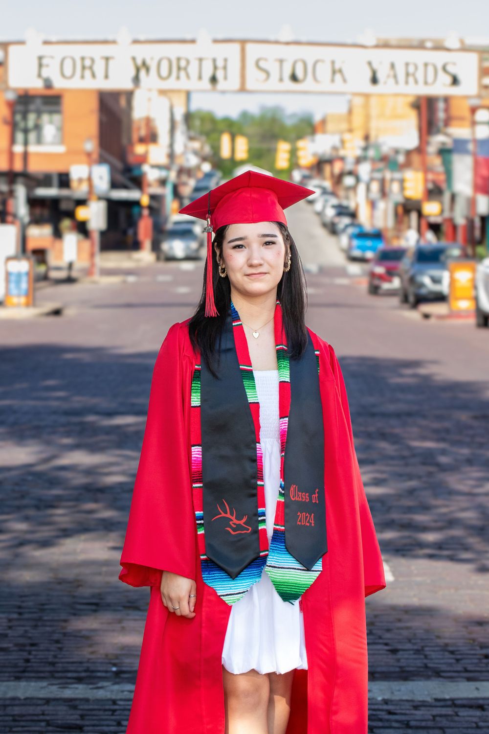 Graduate in red cap and gown posing in the Fort Worth Stockyards historic district.
