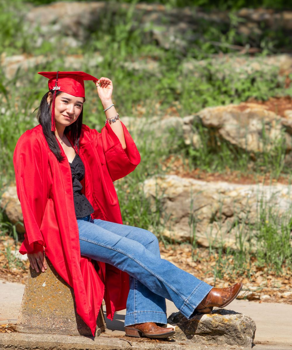 Someone in a bright red jacket and jeans poses playfully on outdoor steps surrounded by greenery.