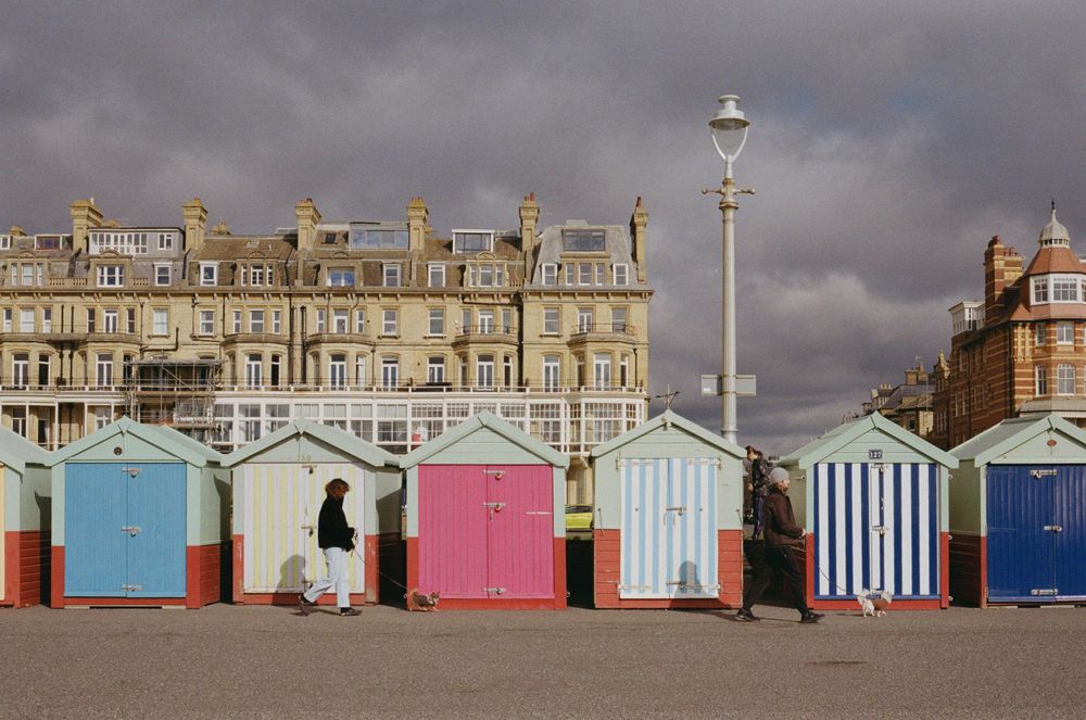 Colorful beach huts lined up along the seafront with Victorian buildings in background.