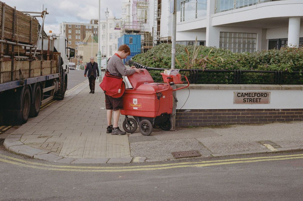 A person with a red cart stands on a street corner near urban buildings.