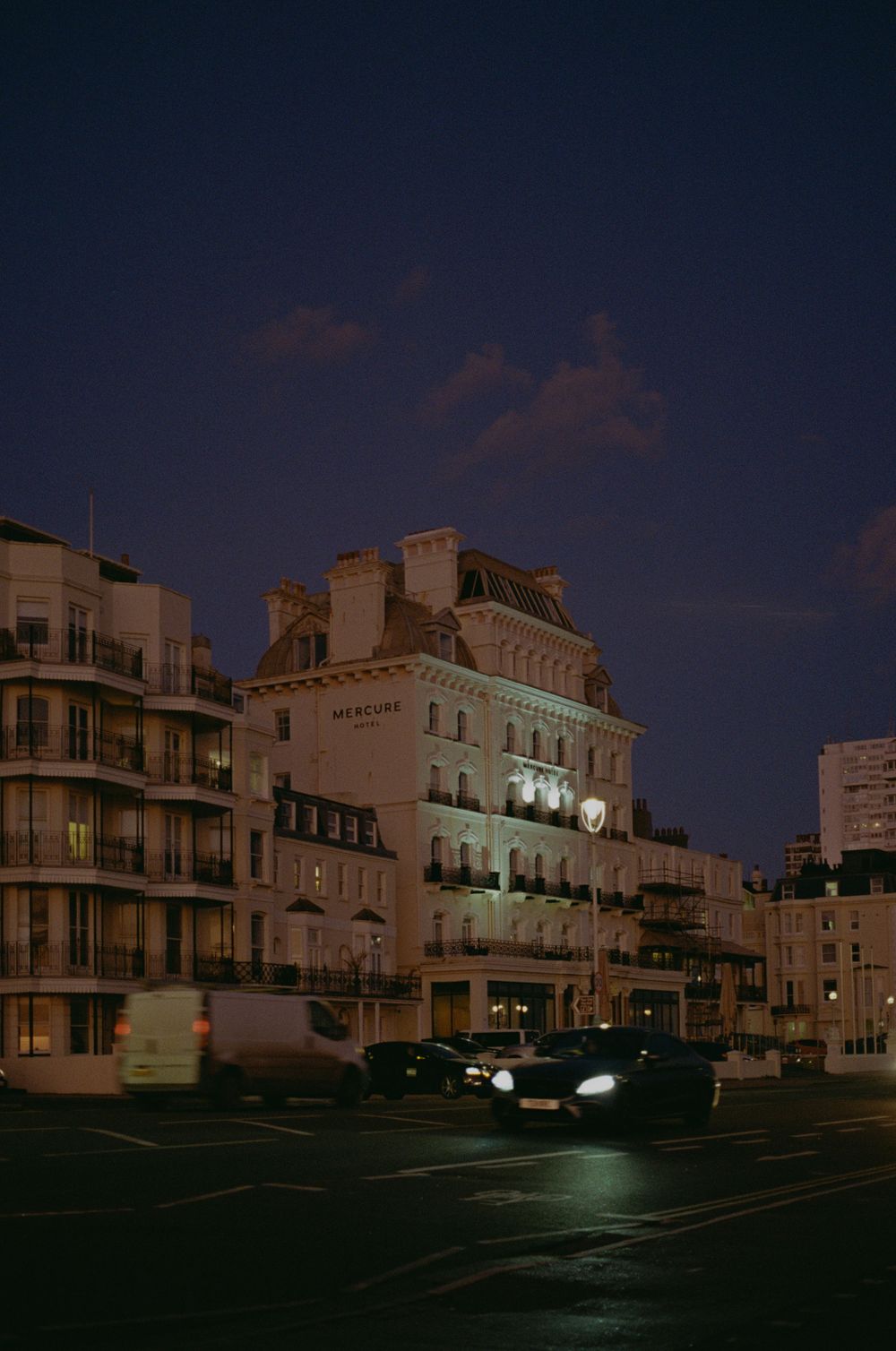 Historic Brighton hotel building lit up at night with parked cars in foreground.