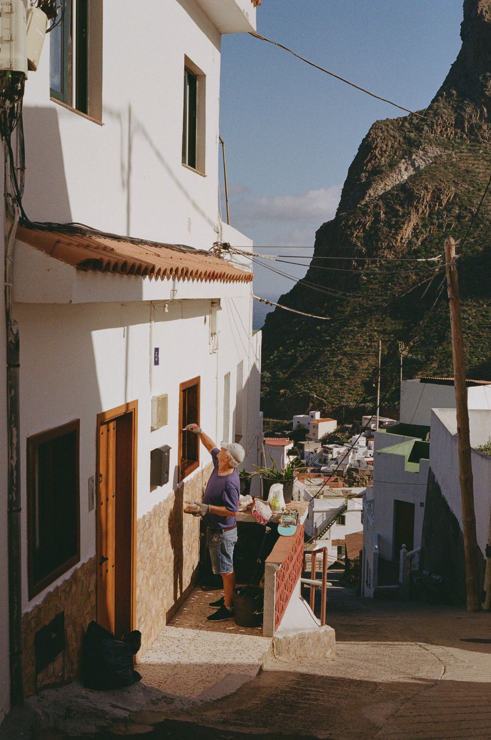 Narrow cobblestone street between white buildings with dramatic mountain backdrop in Mediterranean town.