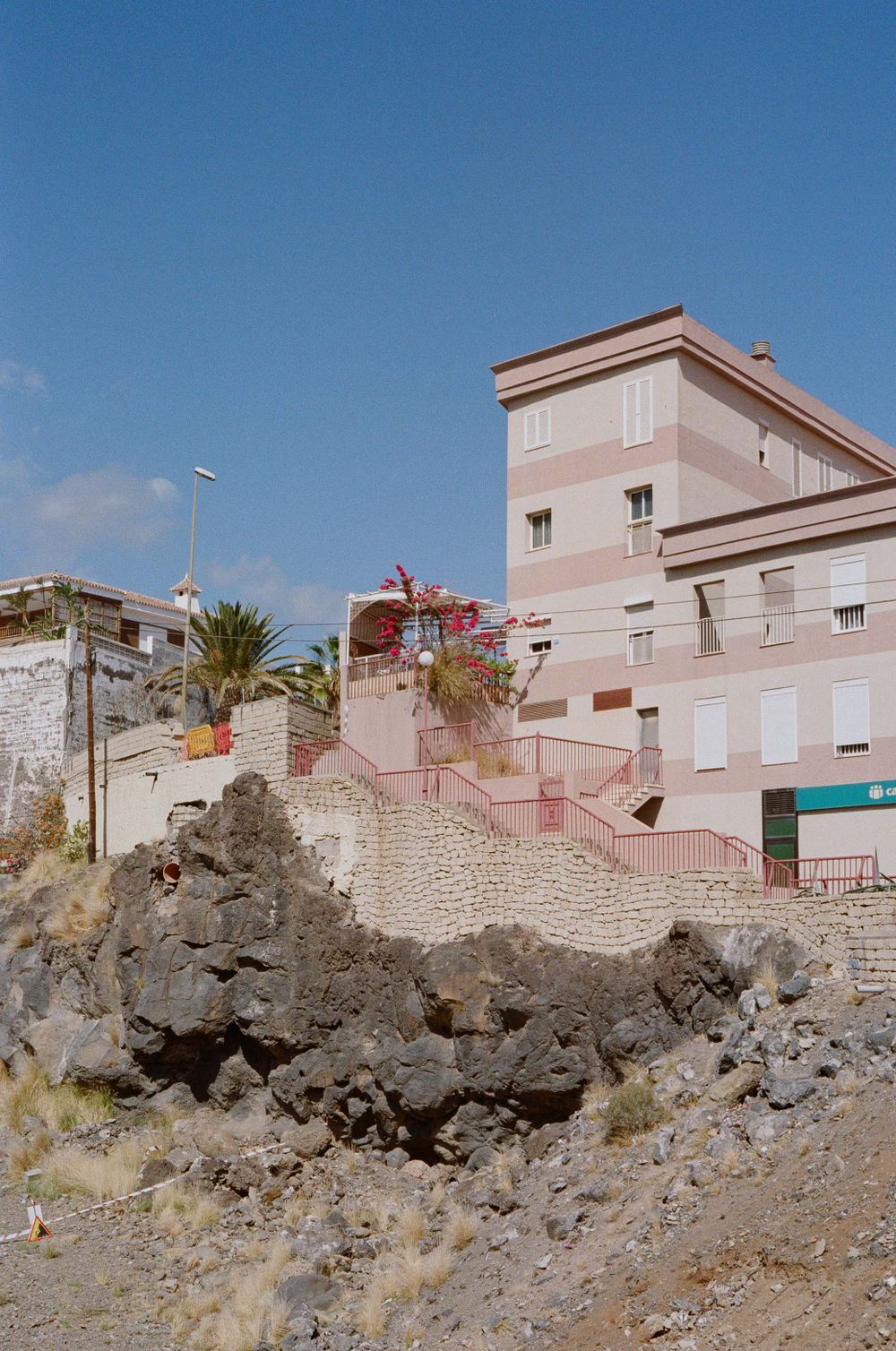 Pink apartment building perched on rocky volcanic cliffs.