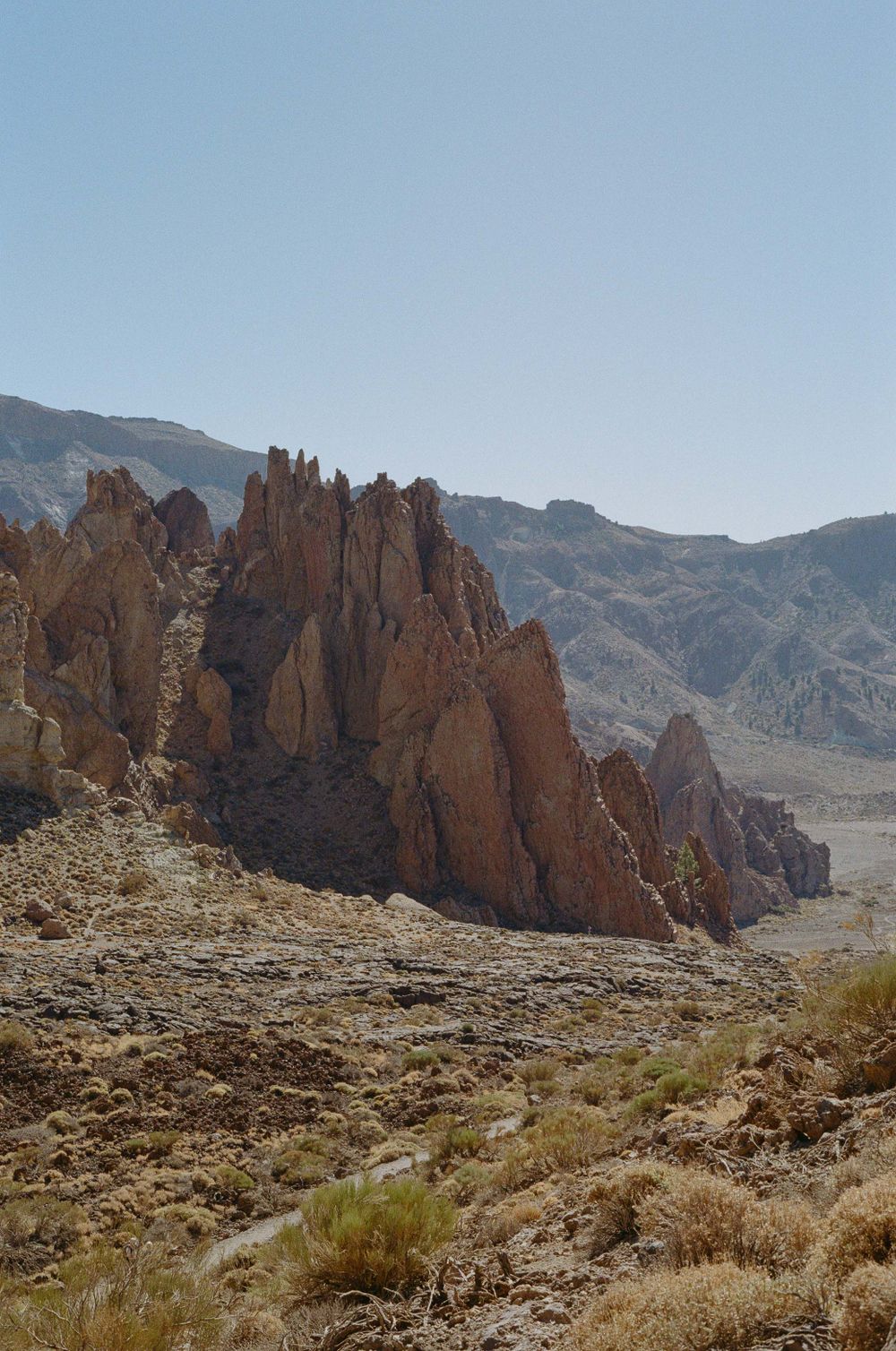 Dramatic rock formations rise from desert terrain against a clear blue sky.