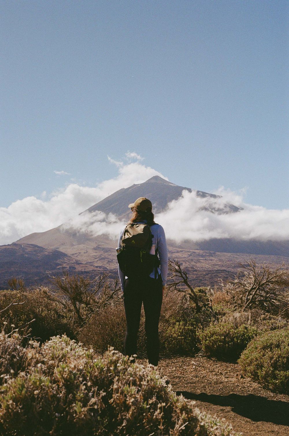 Hiker with backpack gazing at misty mountain peak in the distance.
