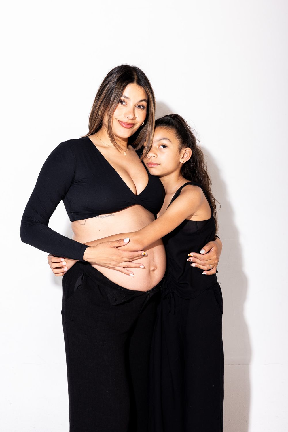 Mother and daughter share an intimate moment in matching black outfits during a maternity photoshoot.