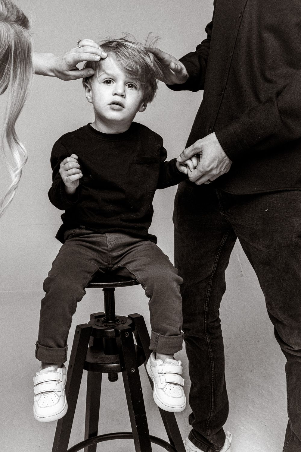 Young child getting a haircut while sitting on a black stool against a gray backdrop.