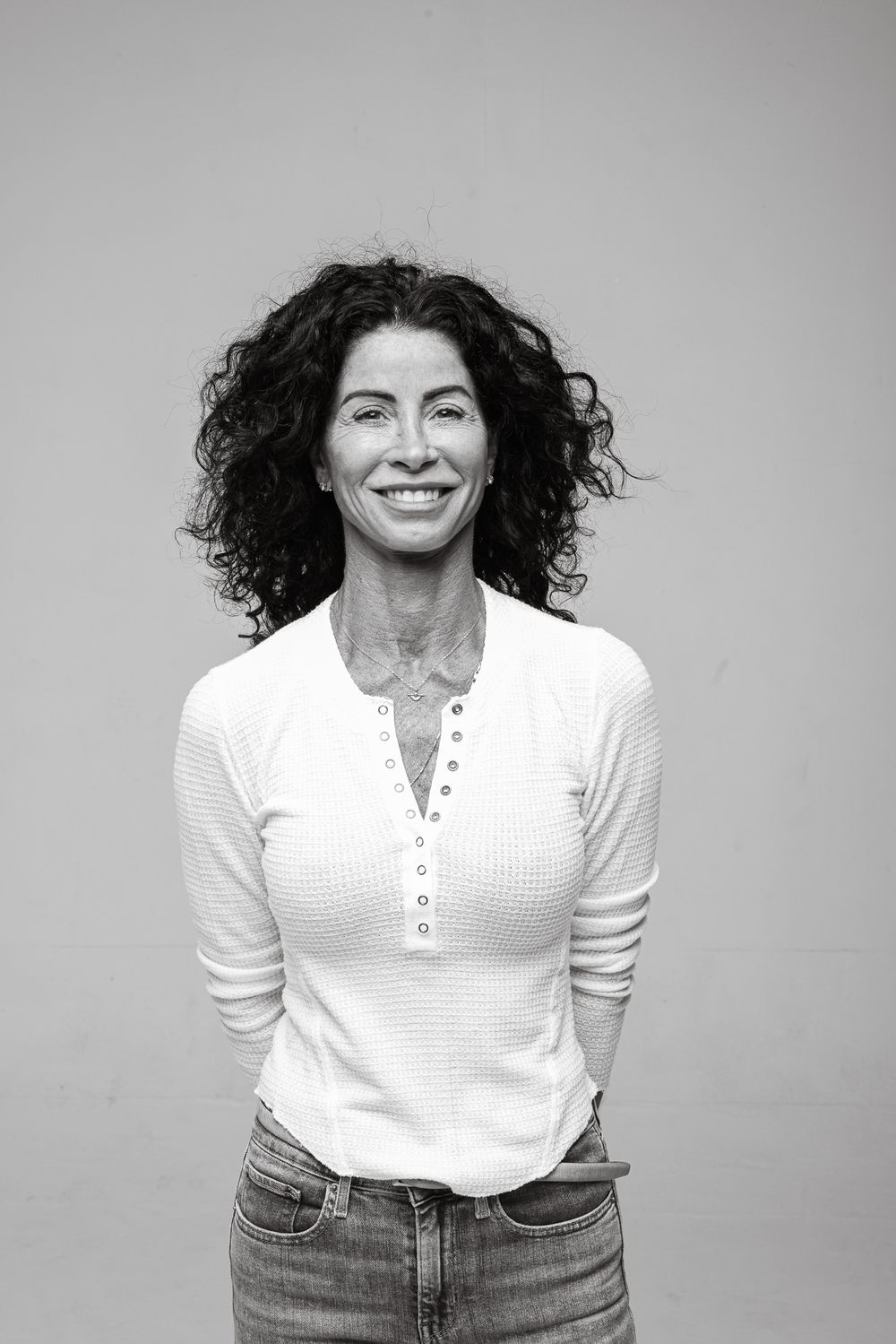 Person wearing a white henley shirt and jeans smiling against a gray background.