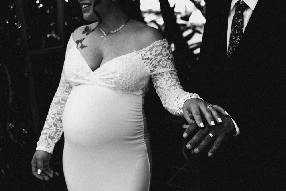 Intimate black and white moment of a pregnant bride in an elegant lace gown.