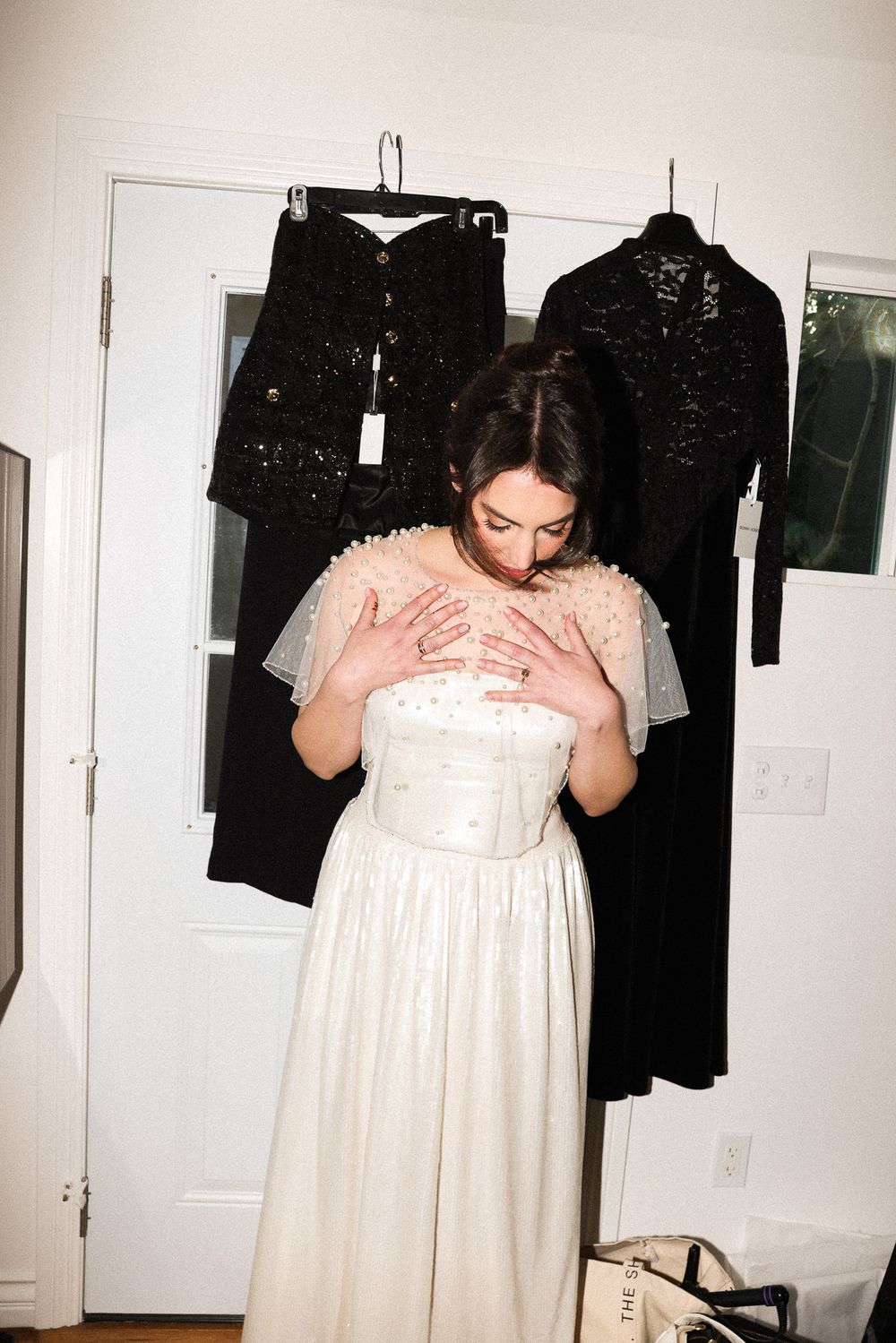 Person in white dress standing in front of hanging black garments.