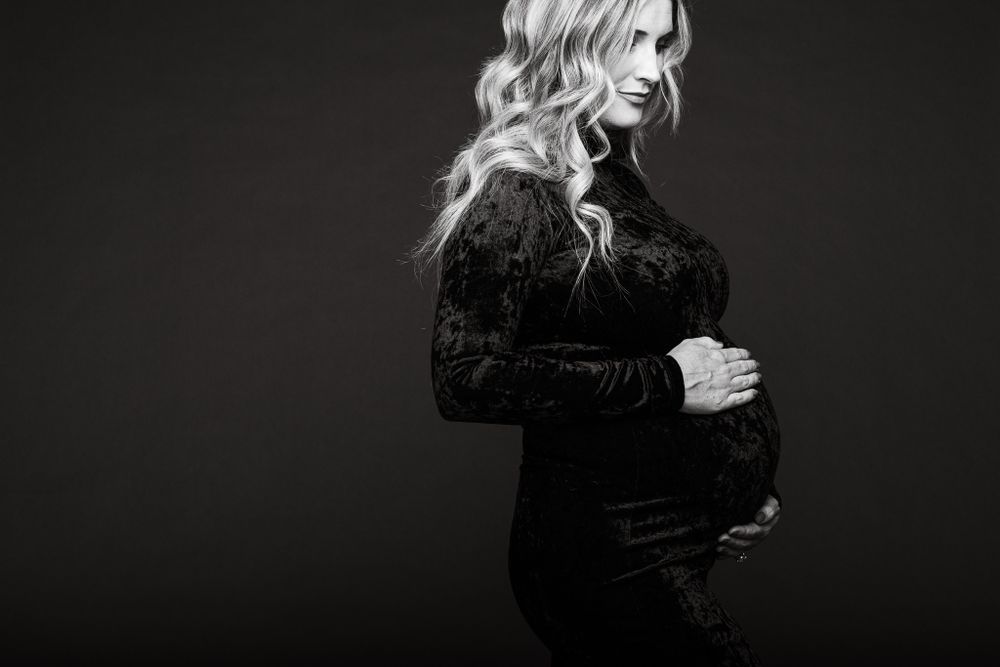 Dramatic black and white maternity portrait against dark background.