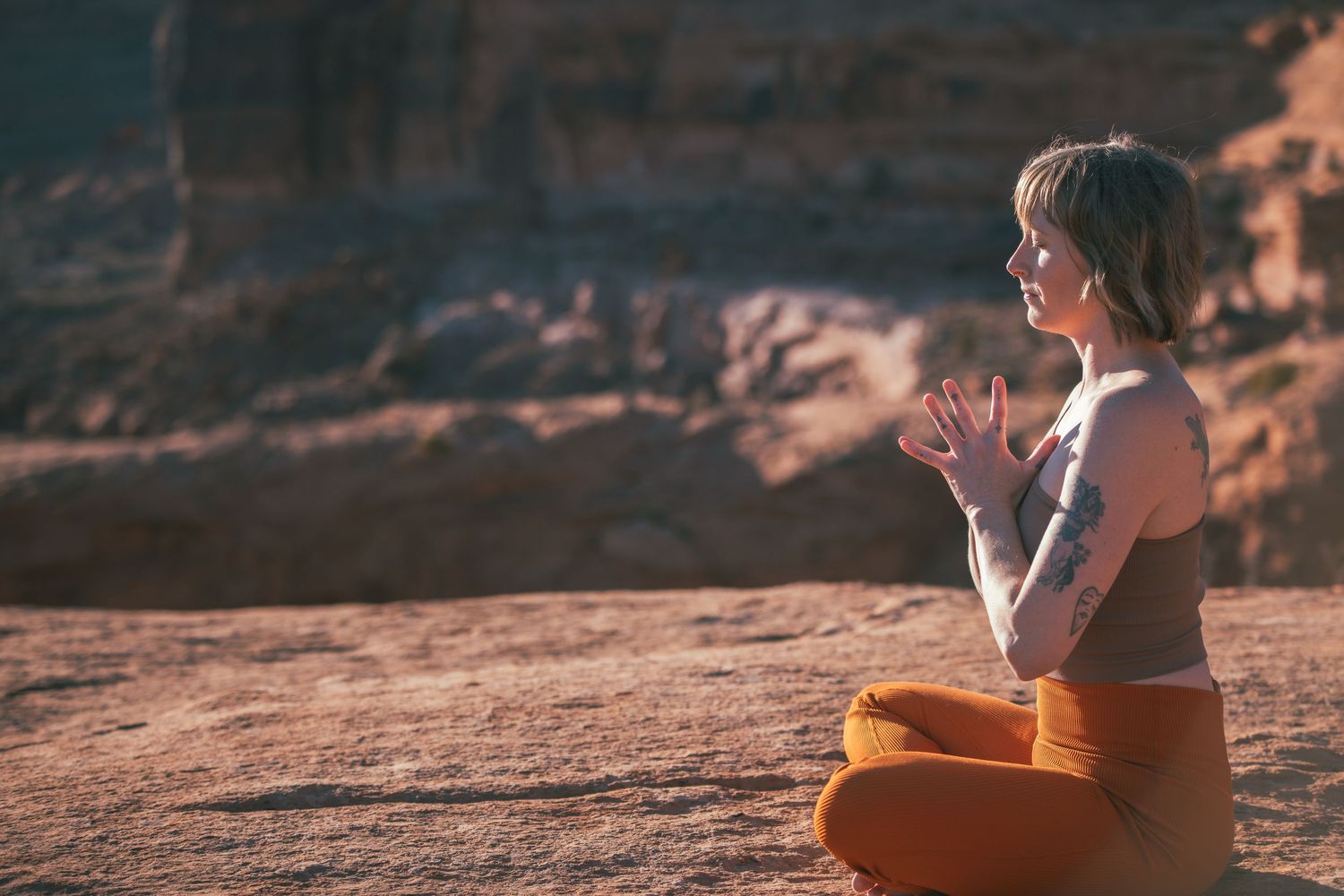 Person meditating on red rock formation at sunset in desert landscape.
