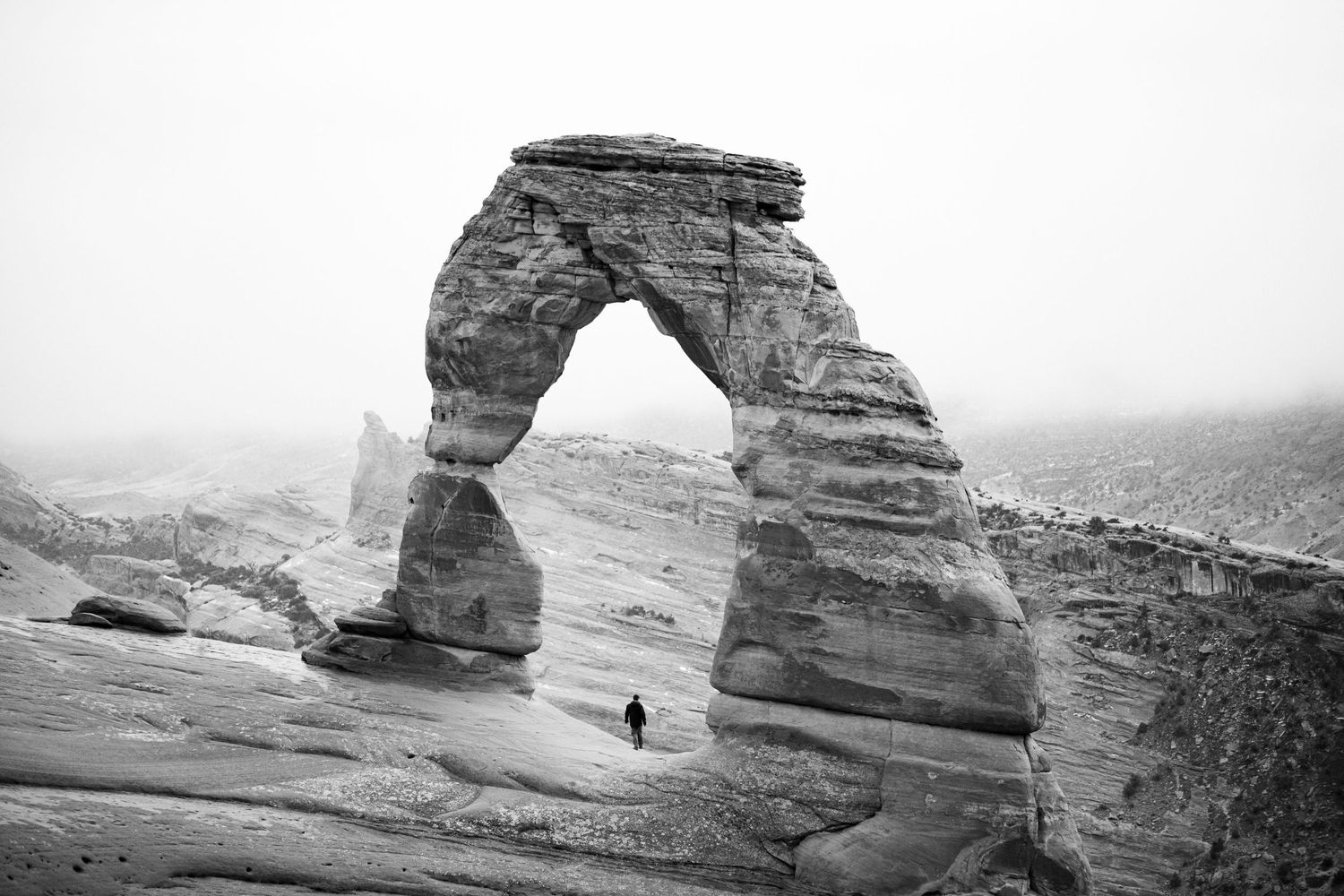 Delicate Arch towers over a small figure in Arches National Park, captured in black and white.