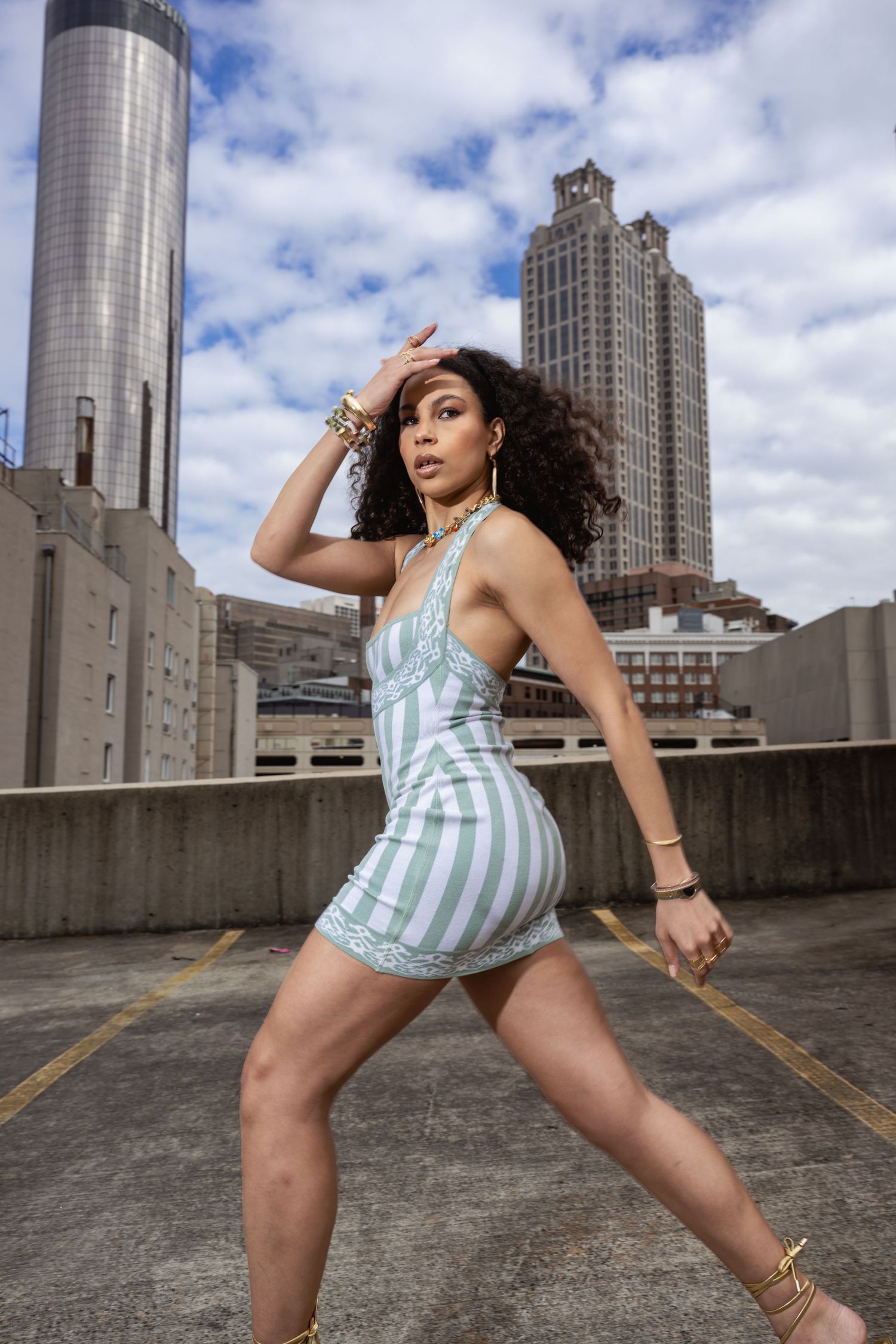 Urban fashion shoot with model in striped Alaia dress posing against city architecture and blue sky.