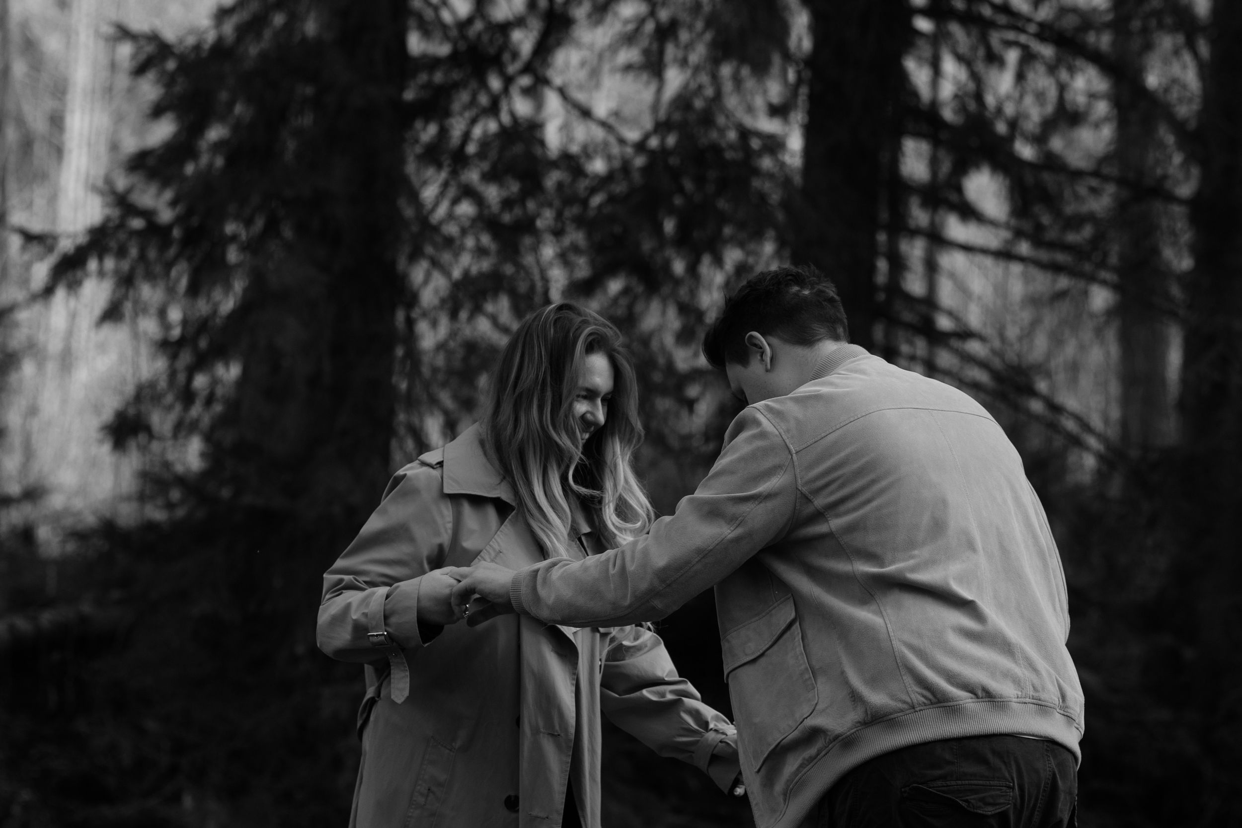 A romantic black and white moment between a couple in a moody forest setting.