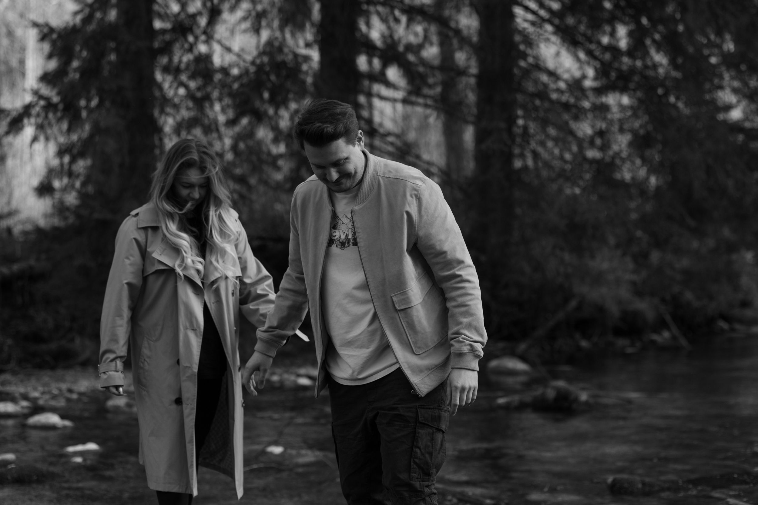 A couple enjoying a walk together beside a stream in a misty forest landscape.