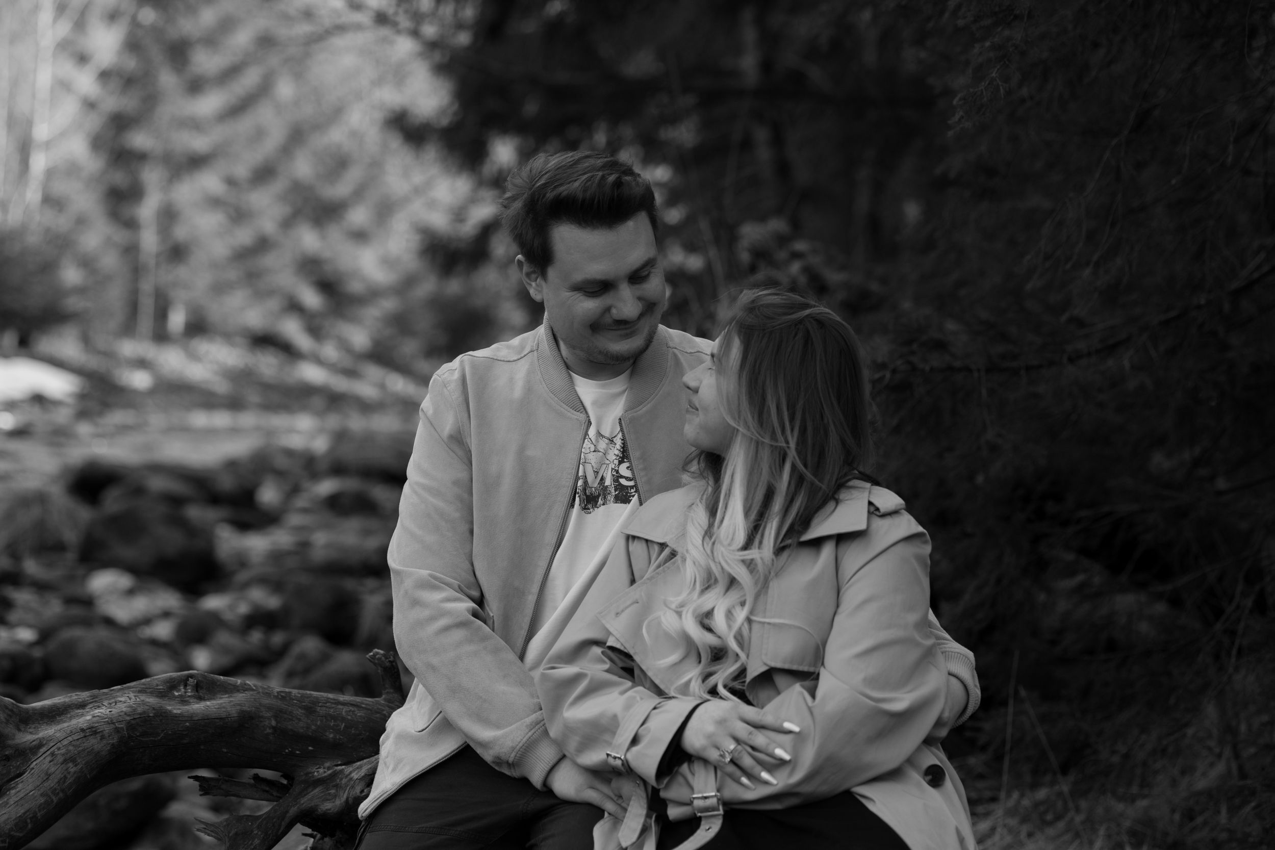 A romantic black and white photo of a couple sitting together outdoors in a forest setting.