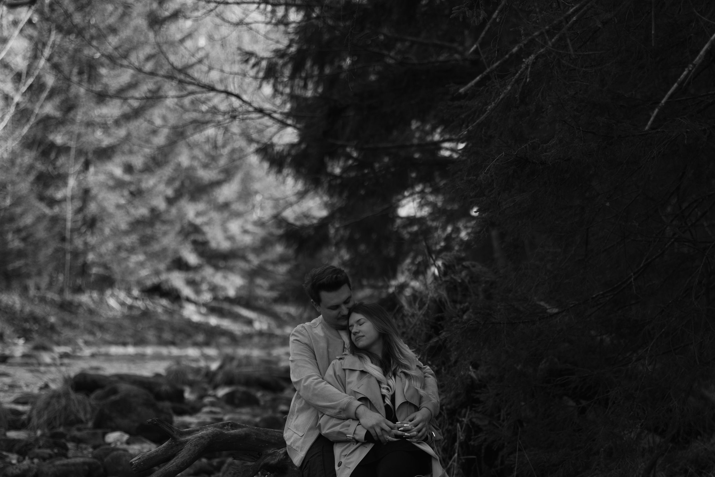 A couple shares an intimate moment together on a forest path in dramatic black and white.