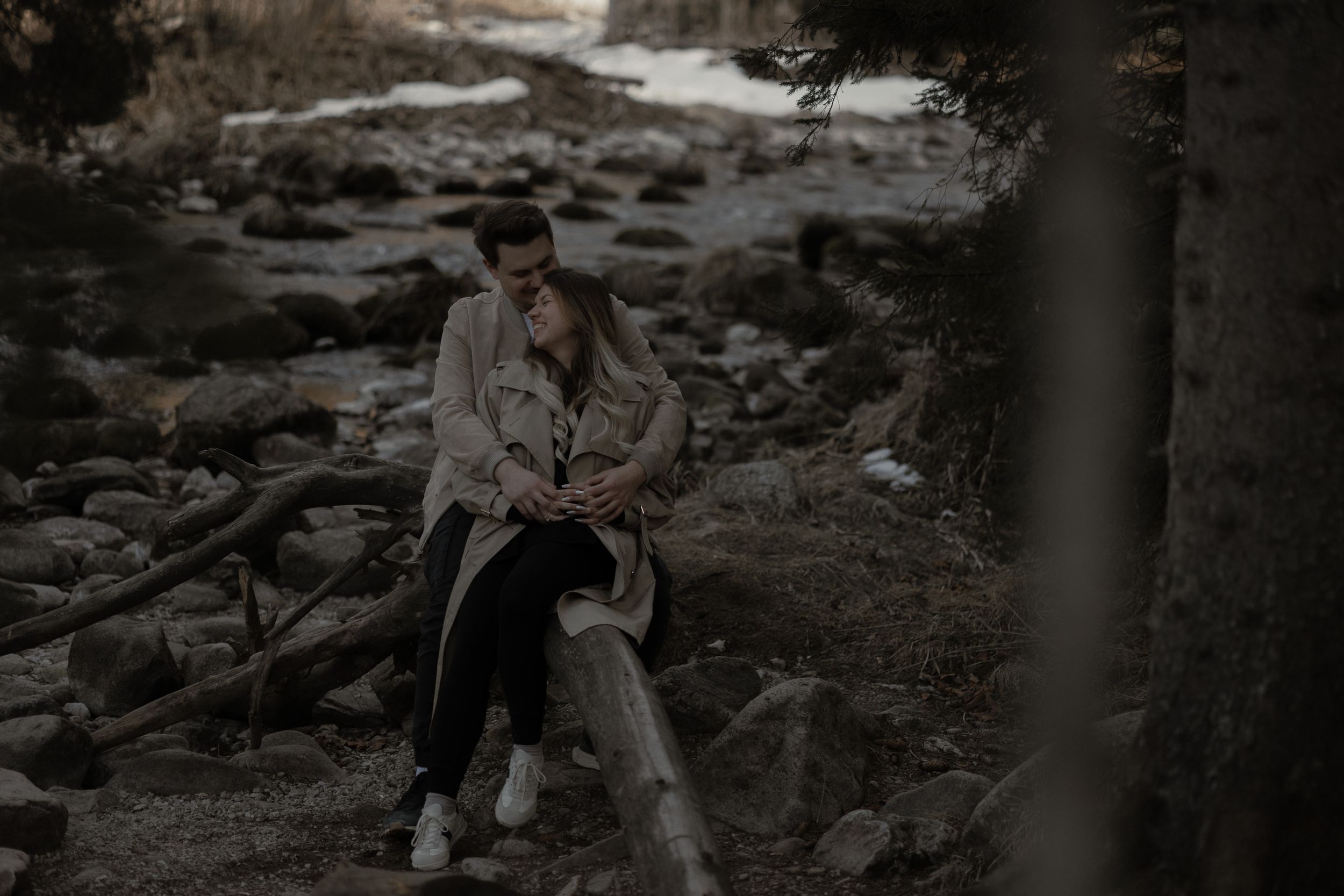 Person in casual attire sits thoughtfully on rocky terrain at dusk in a moody, atmospheric setting.
