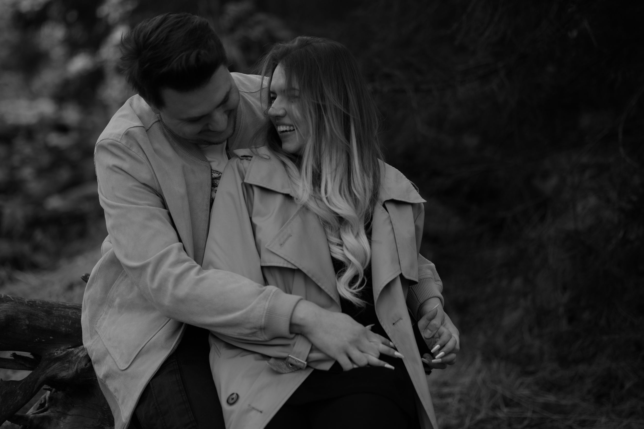 A couple in matching light colored coats share an intimate moment together in black and white photography.