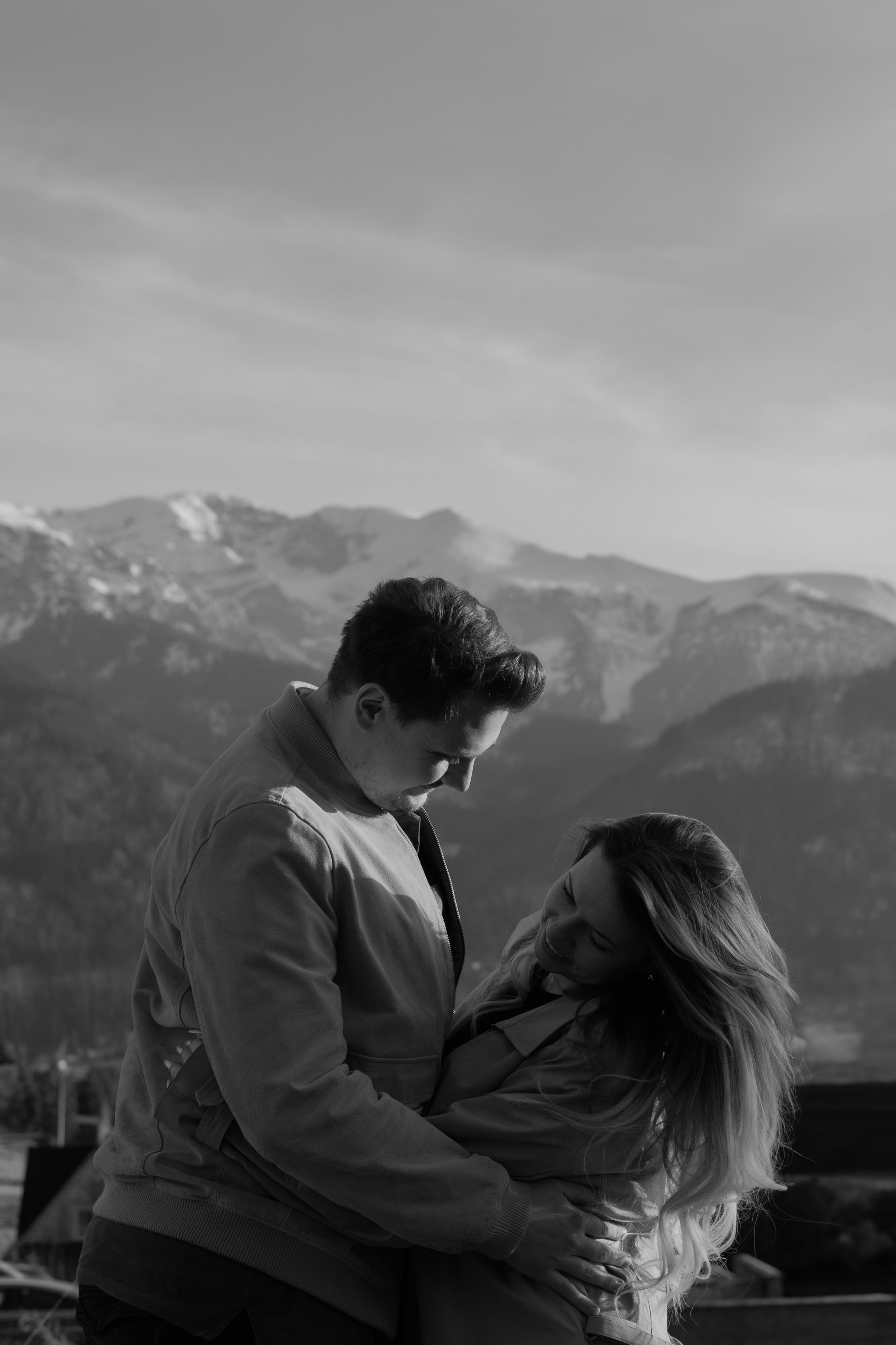 Black and white romantic portrait of a couple embracing with majestic snow-capped mountains in the background.