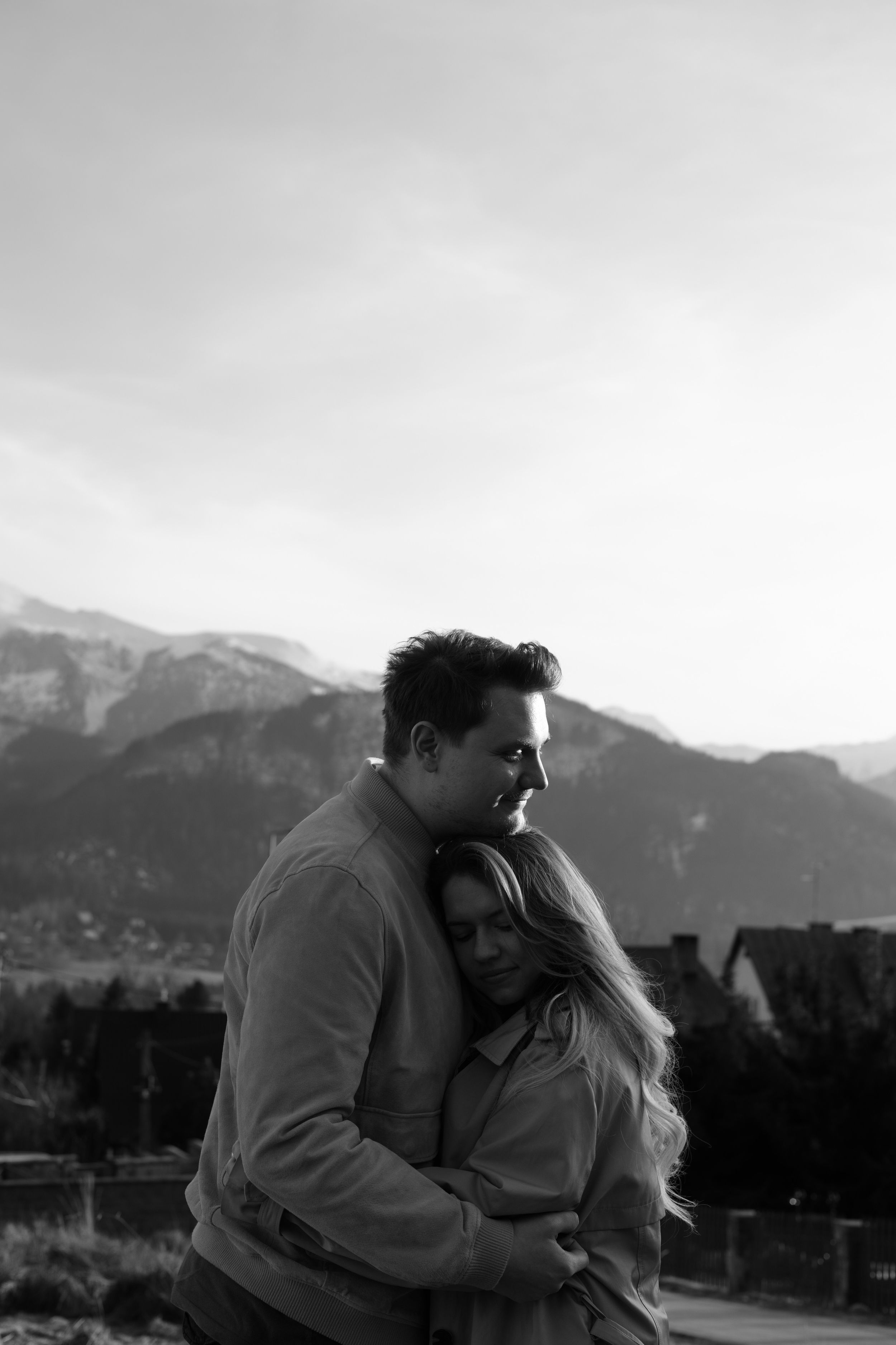 A couple embracing against a backdrop of snow-capped mountains on an overcast day.