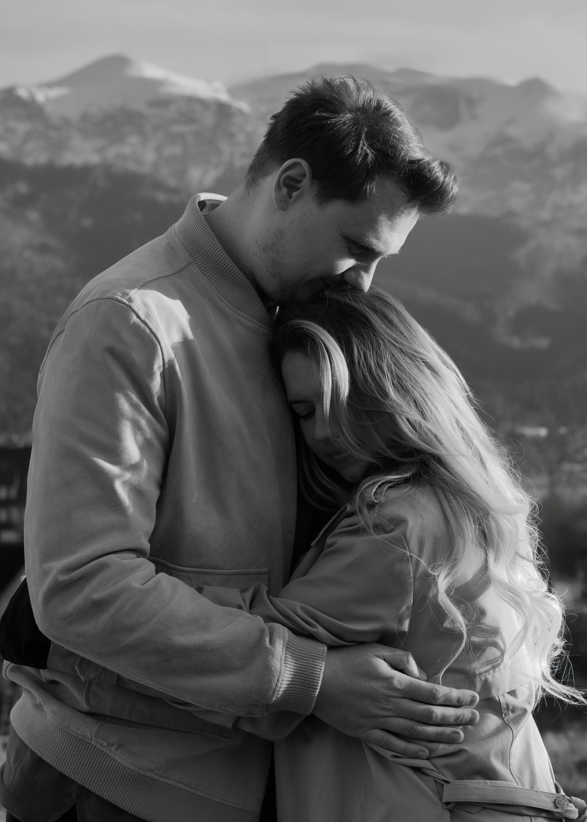 A romantic black and white portrait of a couple sharing an intimate moment with mountain peaks in the distance.