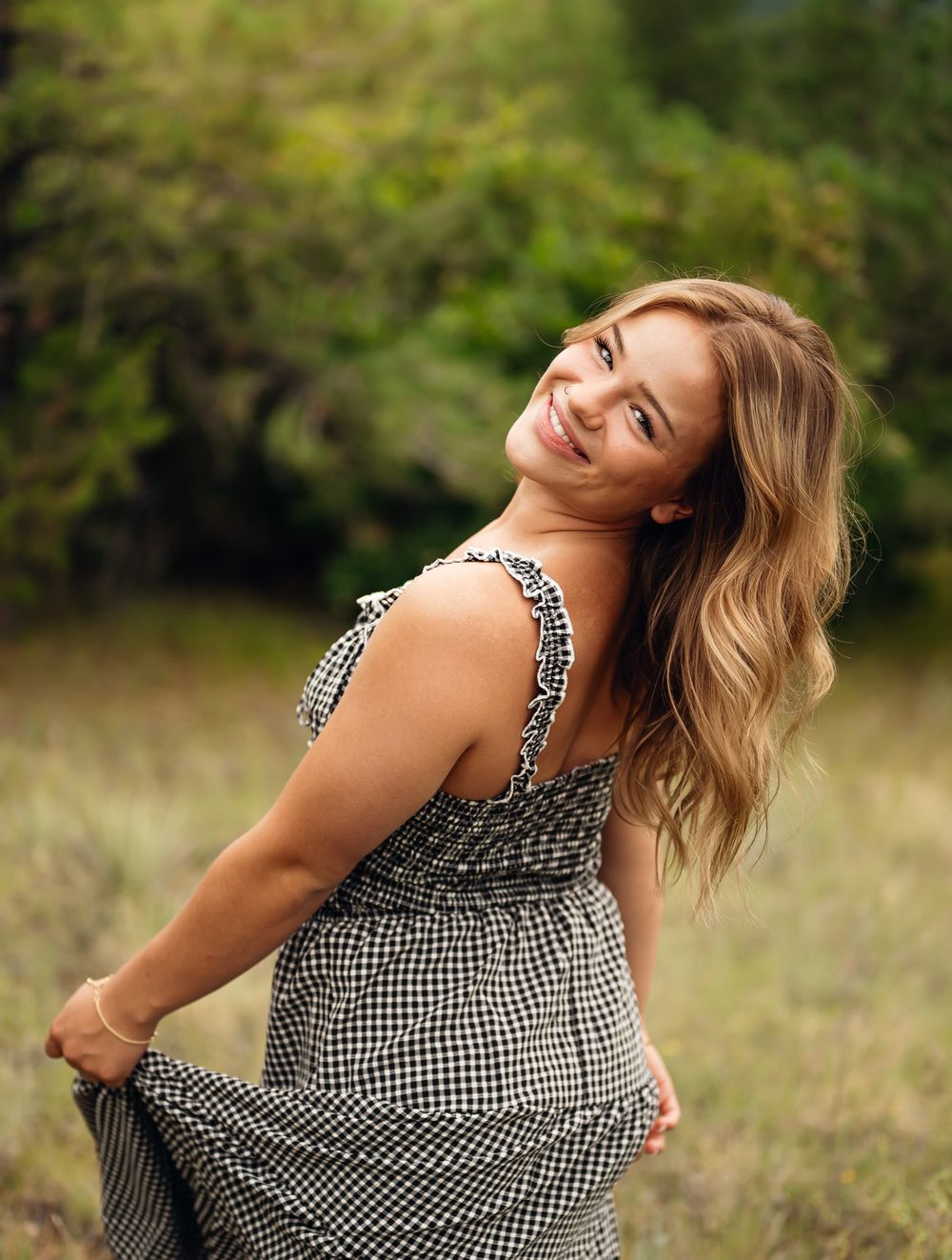 A joyful portrait in a black and white gingham dress twirling in a sunny meadow with blurred greenery background.