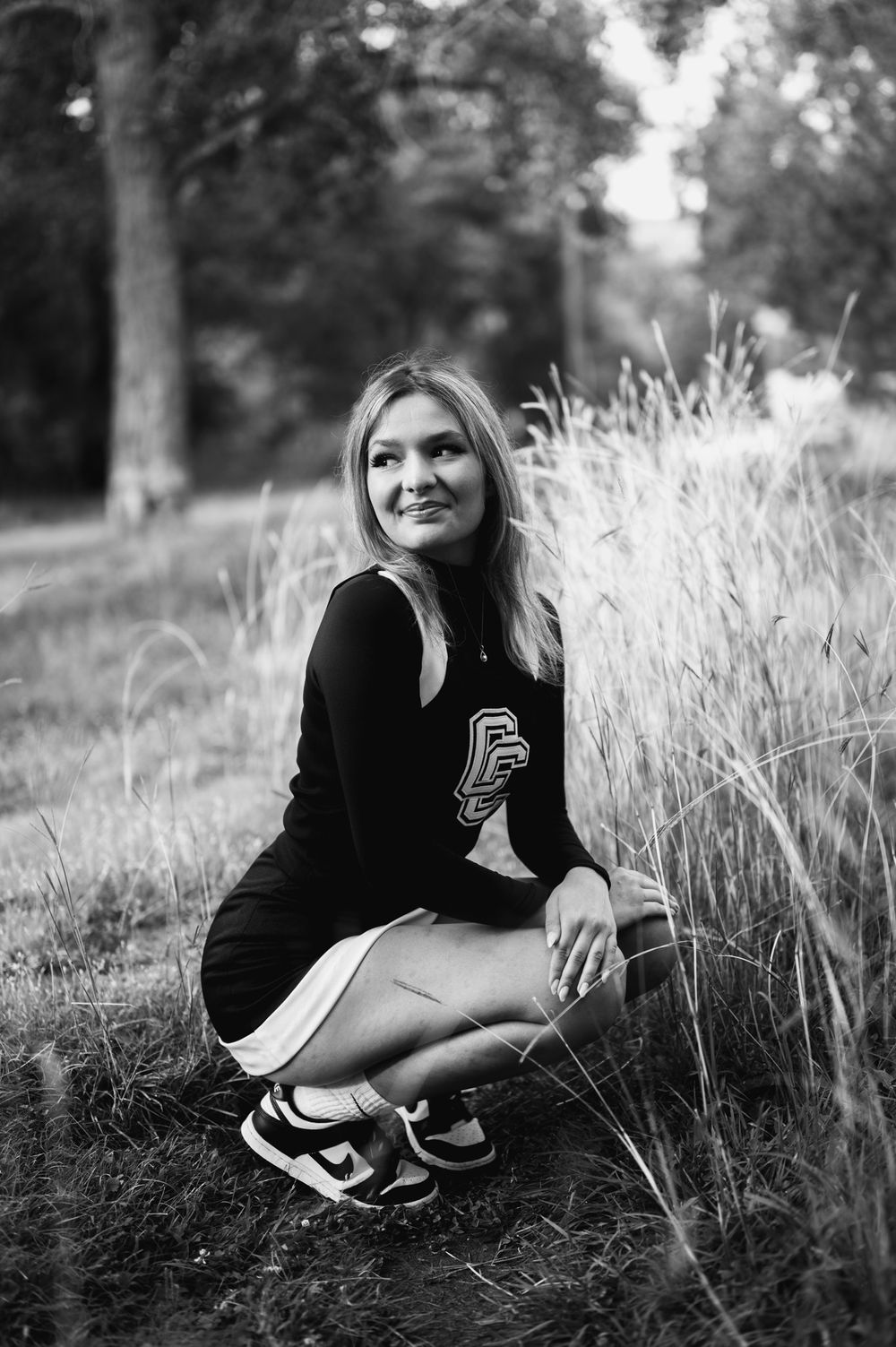 Black and white photo series of a person sitting in tall grass wearing a black sweater and athletic shoes.