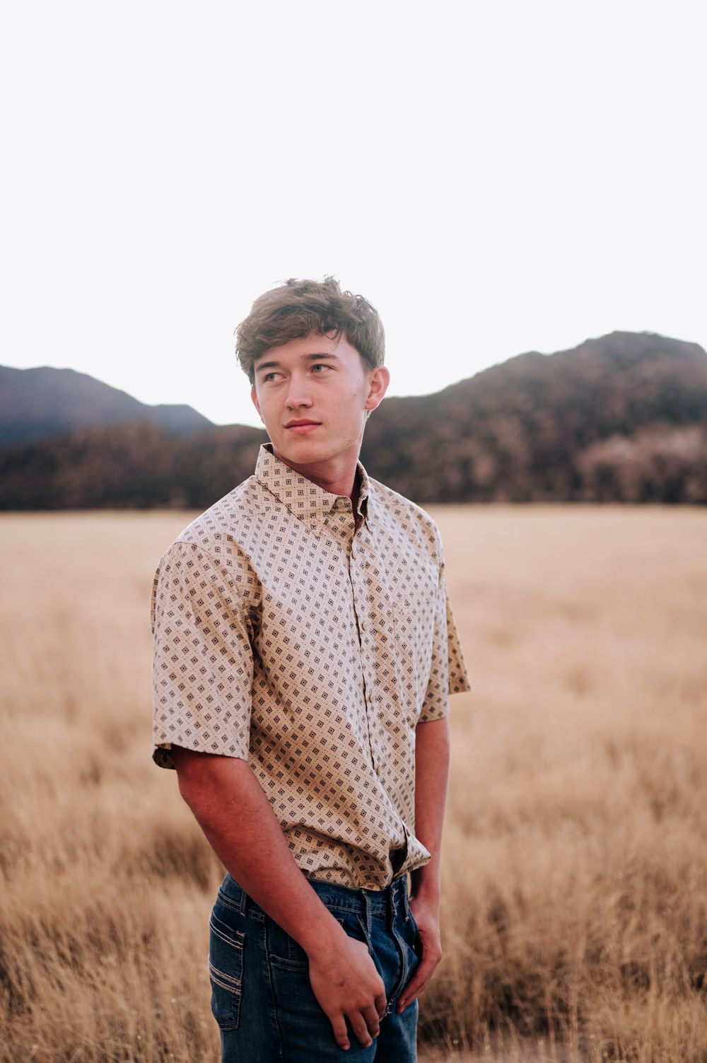 A person wearing a polka dot shirt and jeans stands in a golden wheat field at sunset.