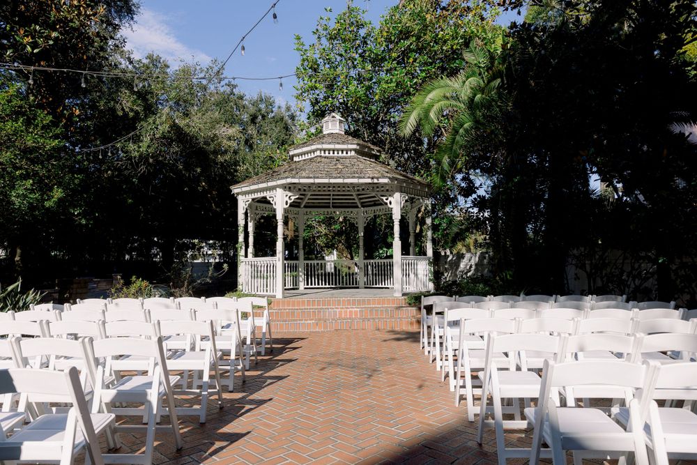 White wedding ceremony setup with gazebo and chairs on brick pathway.