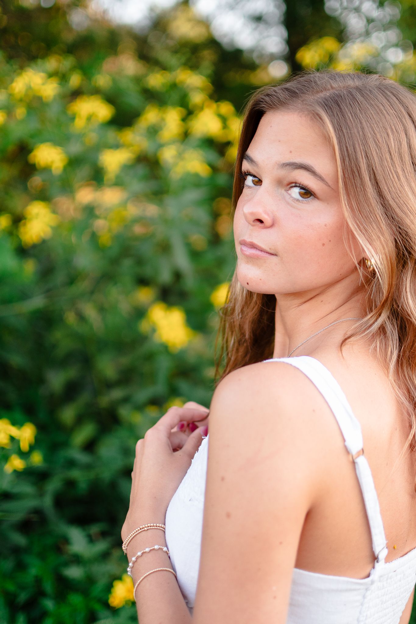 Someone relaxes on grass wearing a beige sweater and light jeans with autumn foliage in the background.