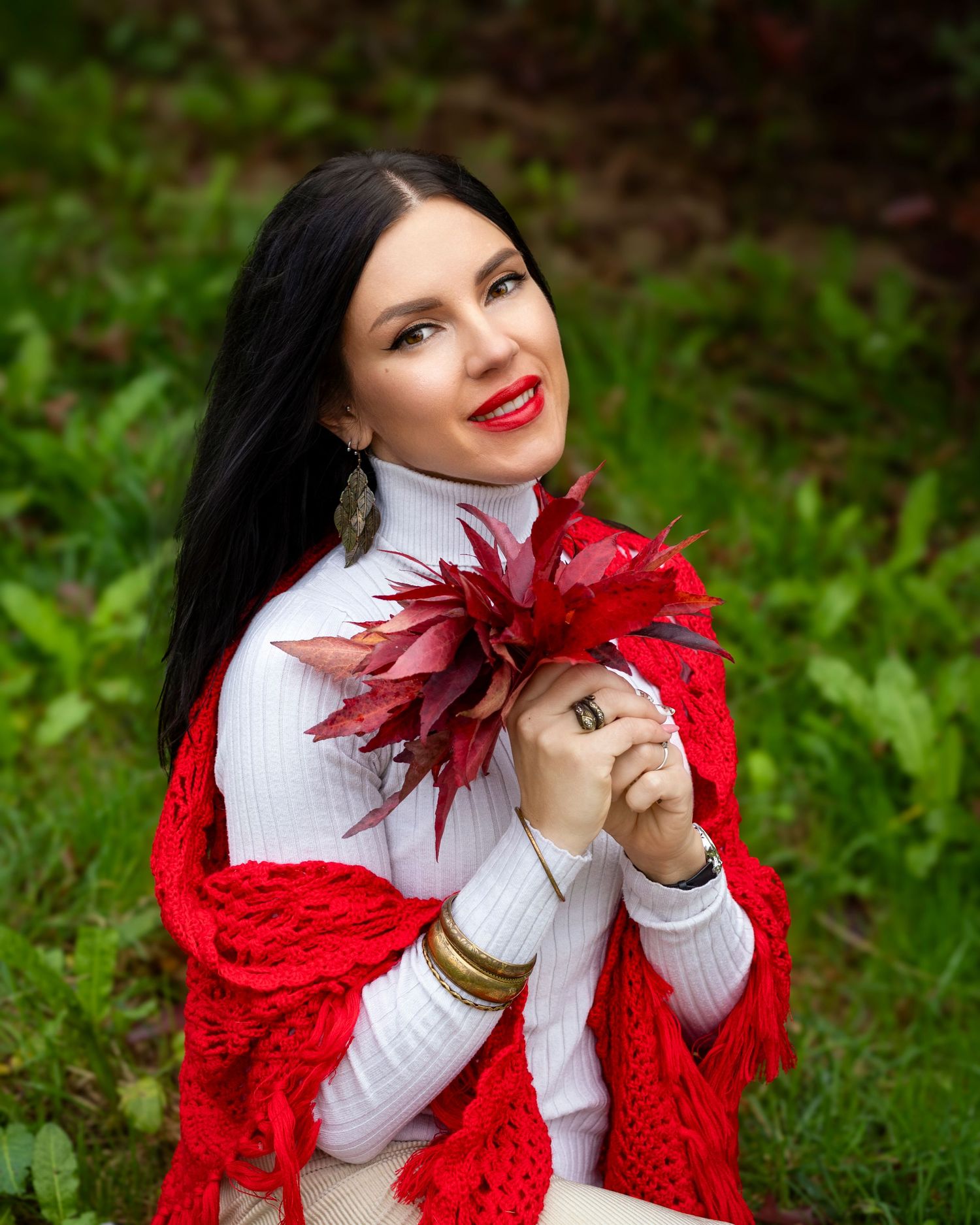 Portrait against green foliage with a white top, red cardigan and vibrant red maple leaves.