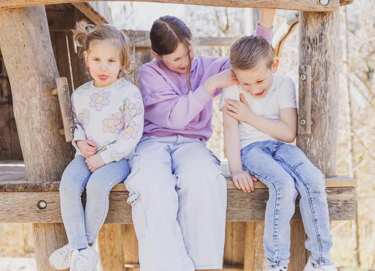 Three people sitting together on a rustic wooden bench. Familie broers en zussen fotografie