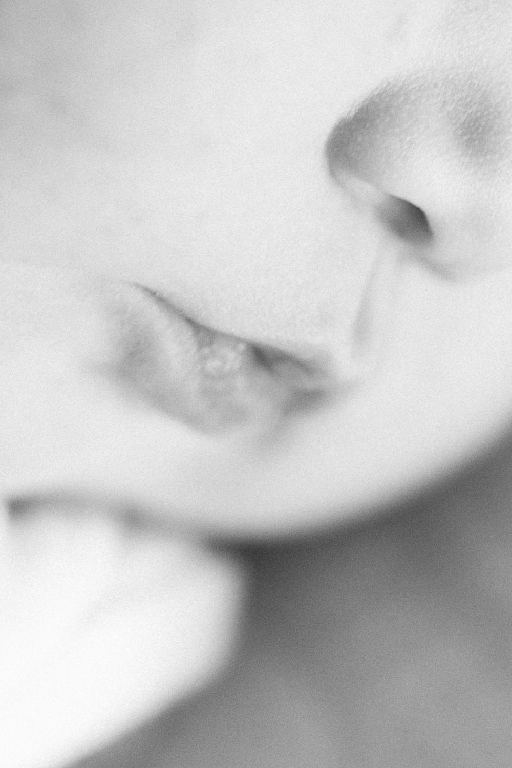 Close-up black and white macro photograph shows partial view of nose and lips in soft focus.