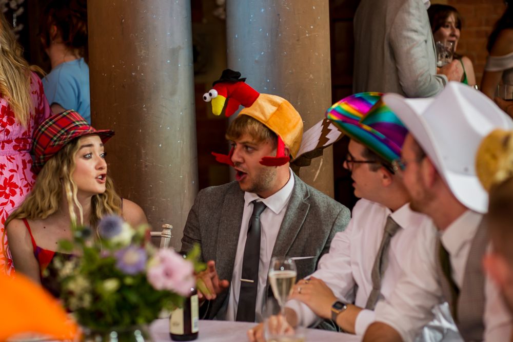 Wedding reception guests wearing colorful party hats celebrate at indoor venue.