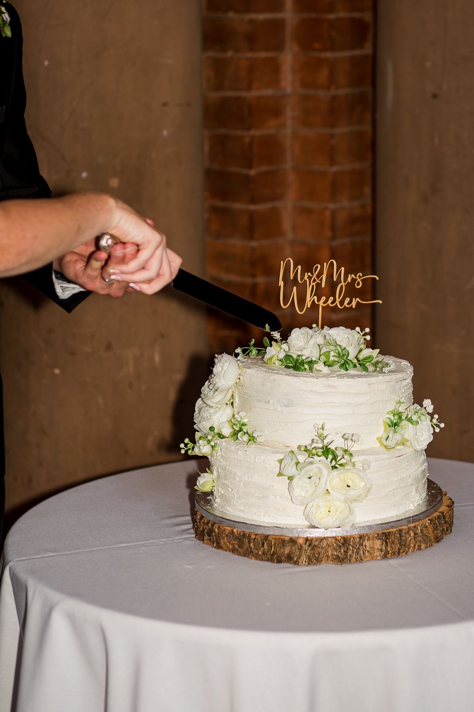 Classic white wedding cake with floral accents being cut on round table.