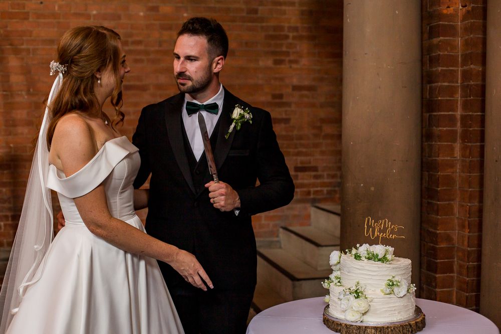 Wedding couple stands together at cake table during reception.