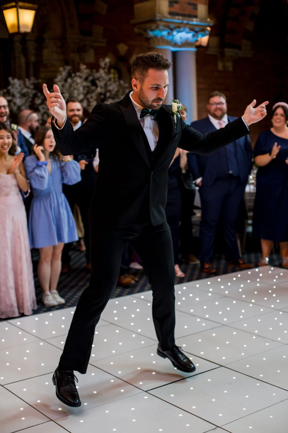 Guests perform choreographed dance moves on a glowing white dance floor at wedding reception.