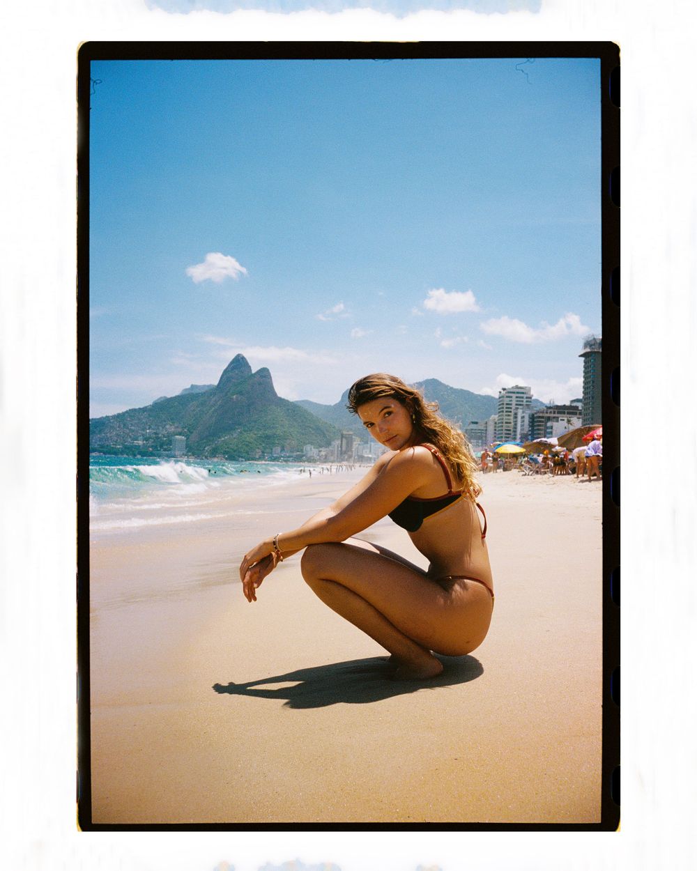 Woman in black bikini posing on Ipanema Beach, Rio de Janeiro, with Two Brothers mountain in background.