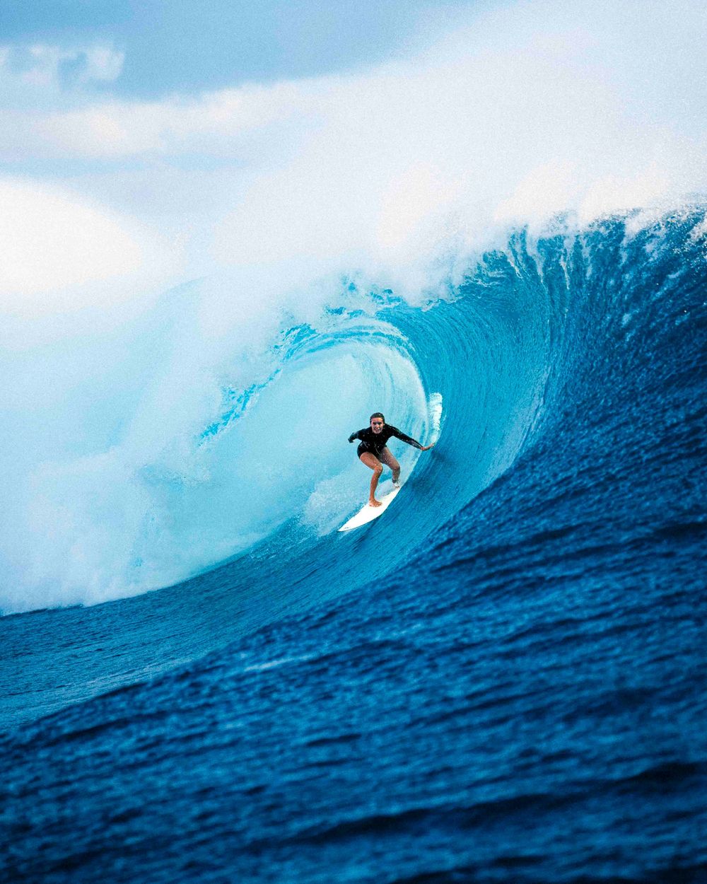 Surfer rides through a massive blue barreling wave in sequence showing progression through the powerful curl.