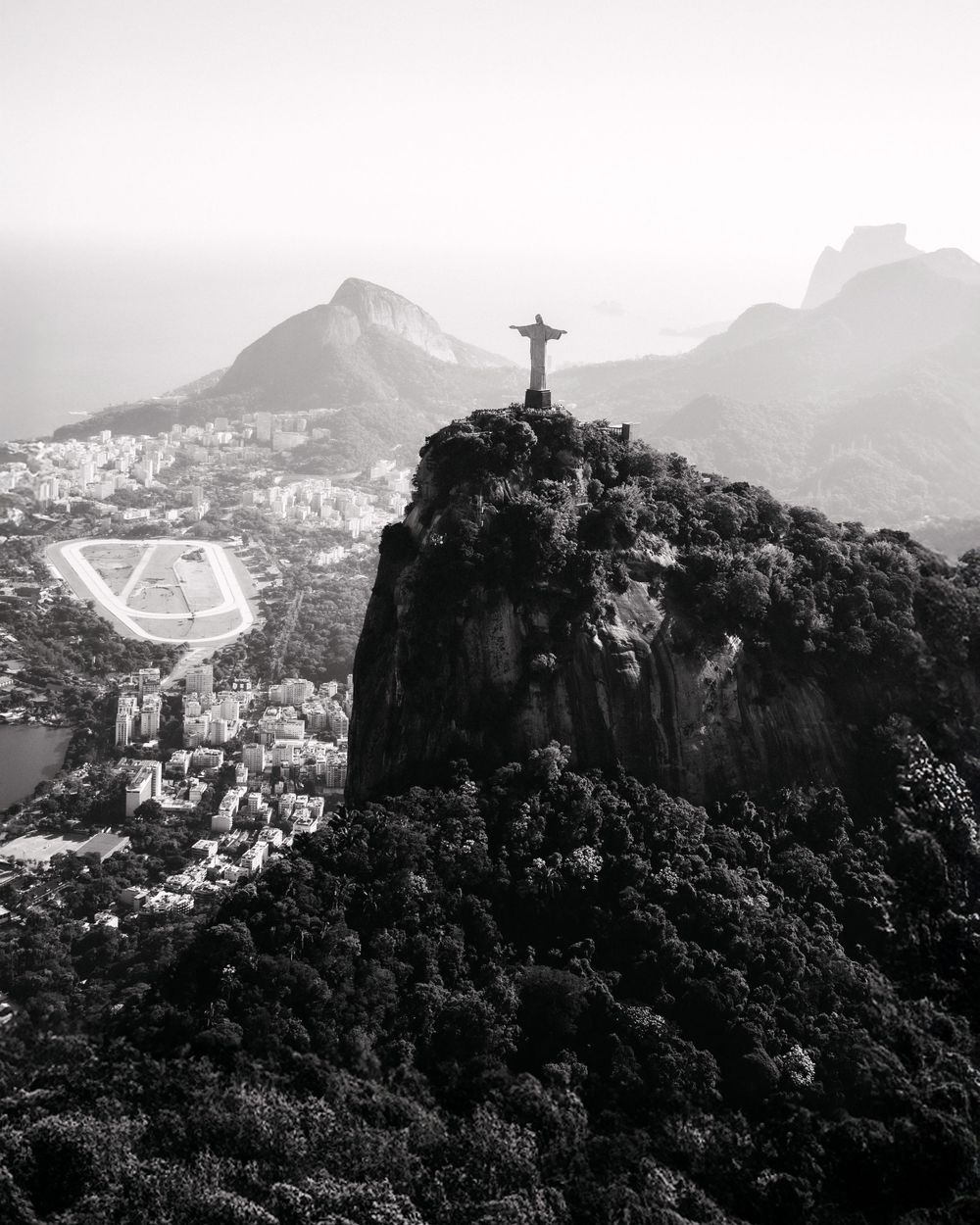 Aerial black and white photo of Christ the Redeemer statue atop Corcovado mountain in Rio de Janeiro, Brazil.